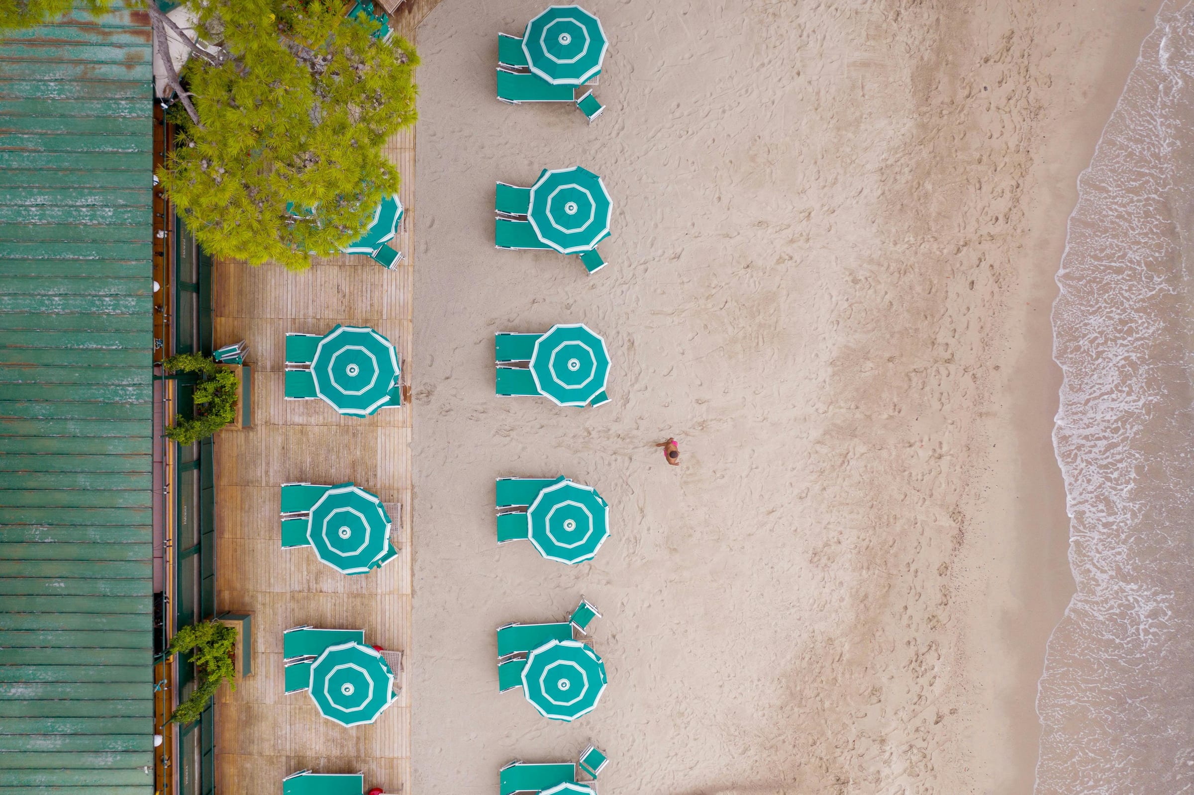 Overhead view of green striped beach umbrellas and loungers on golden Portofino sand