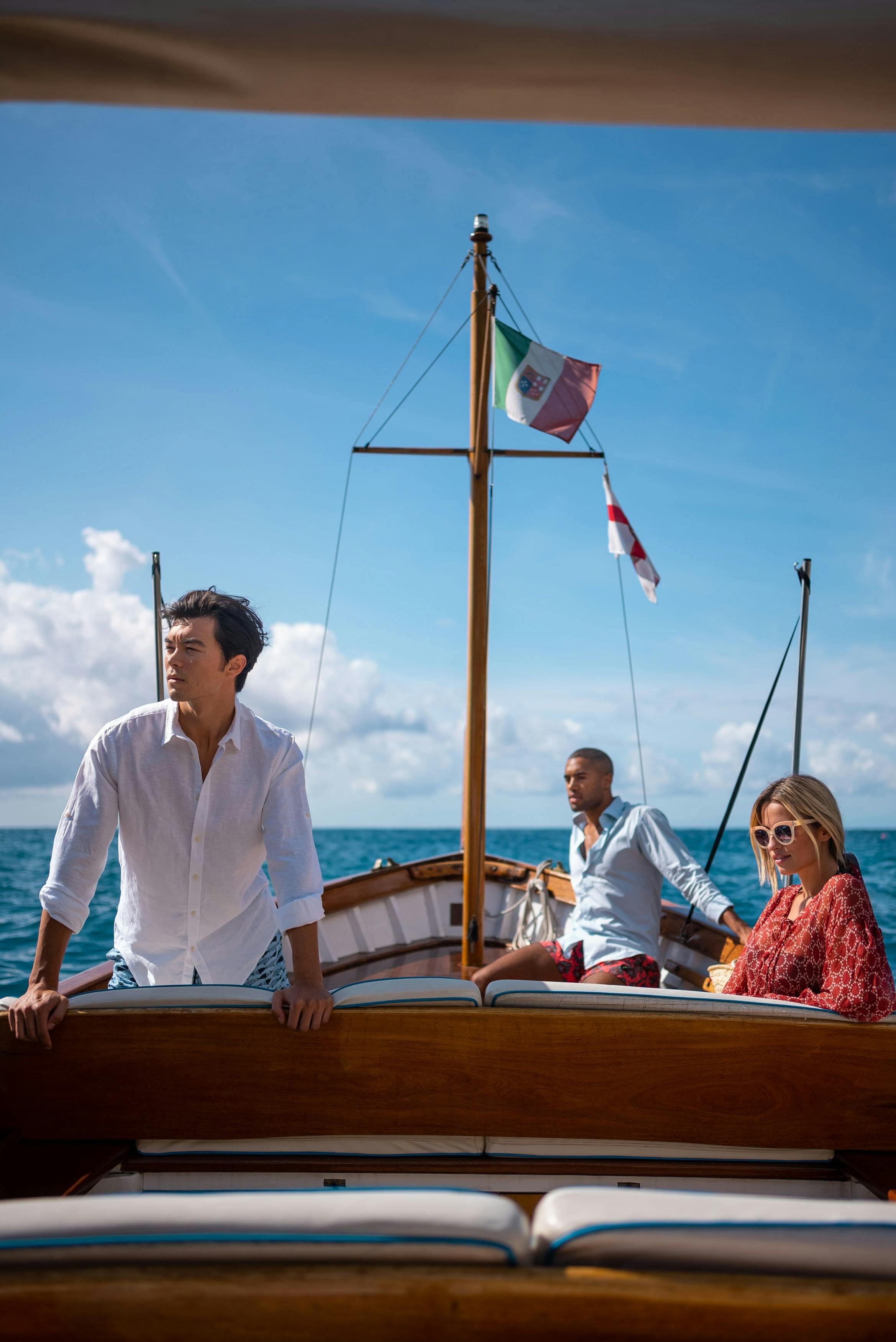 Three friends aboard a varnished wooden boat flying Italian flags on open sea