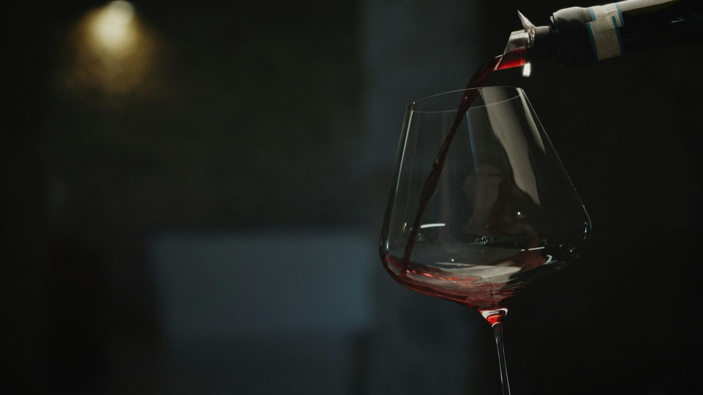 Red wine poured from a bottle into a stemmed glass against darkness
