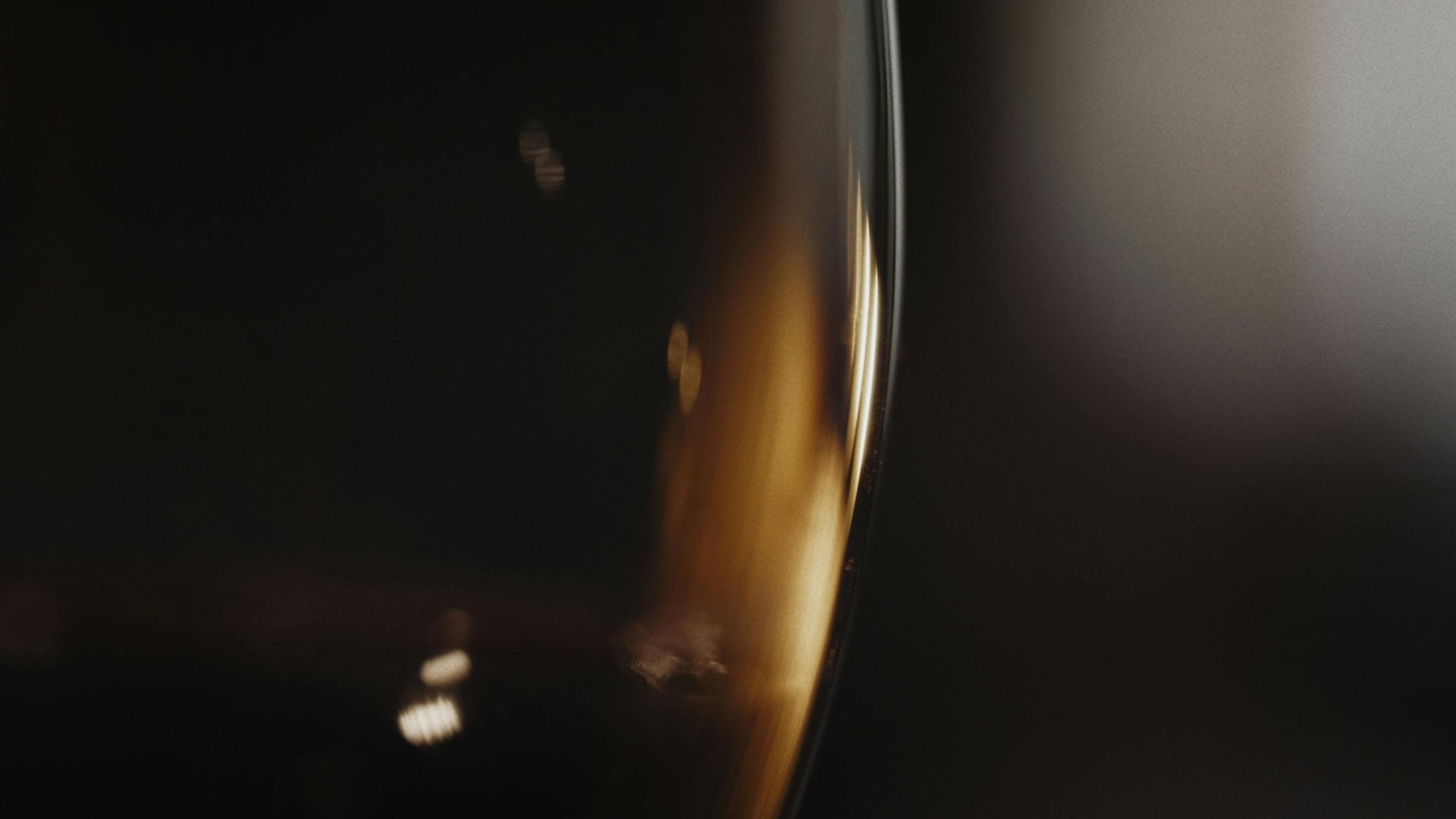 Golden white wine glowing through the curve of a glass in darkness