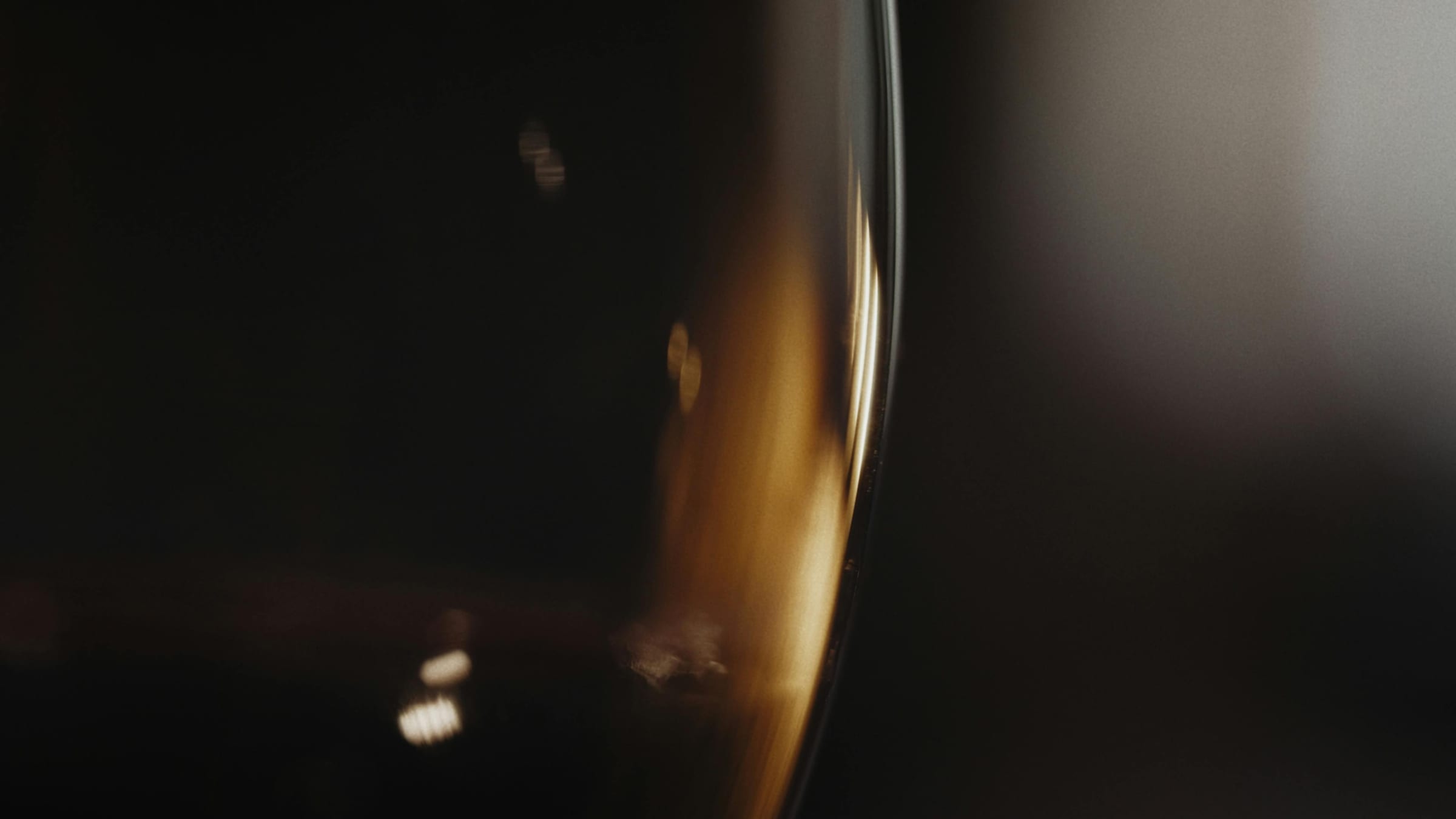 Golden white wine glowing through the curve of a glass in darkness