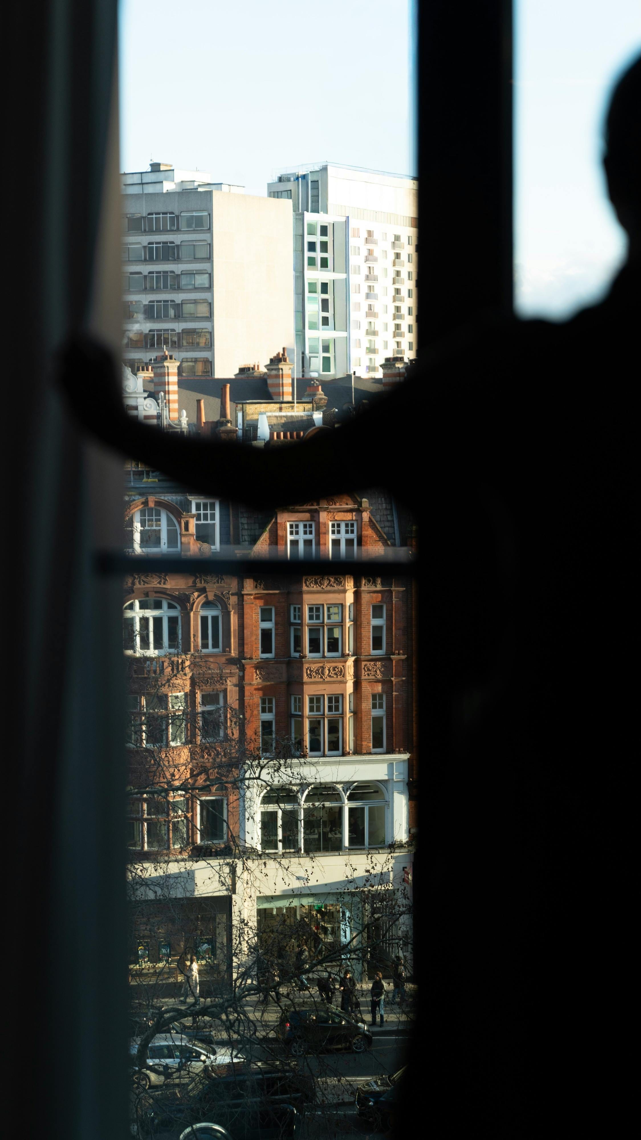 Silhouette at a window overlooking red-brick London townhouses in warm daylight