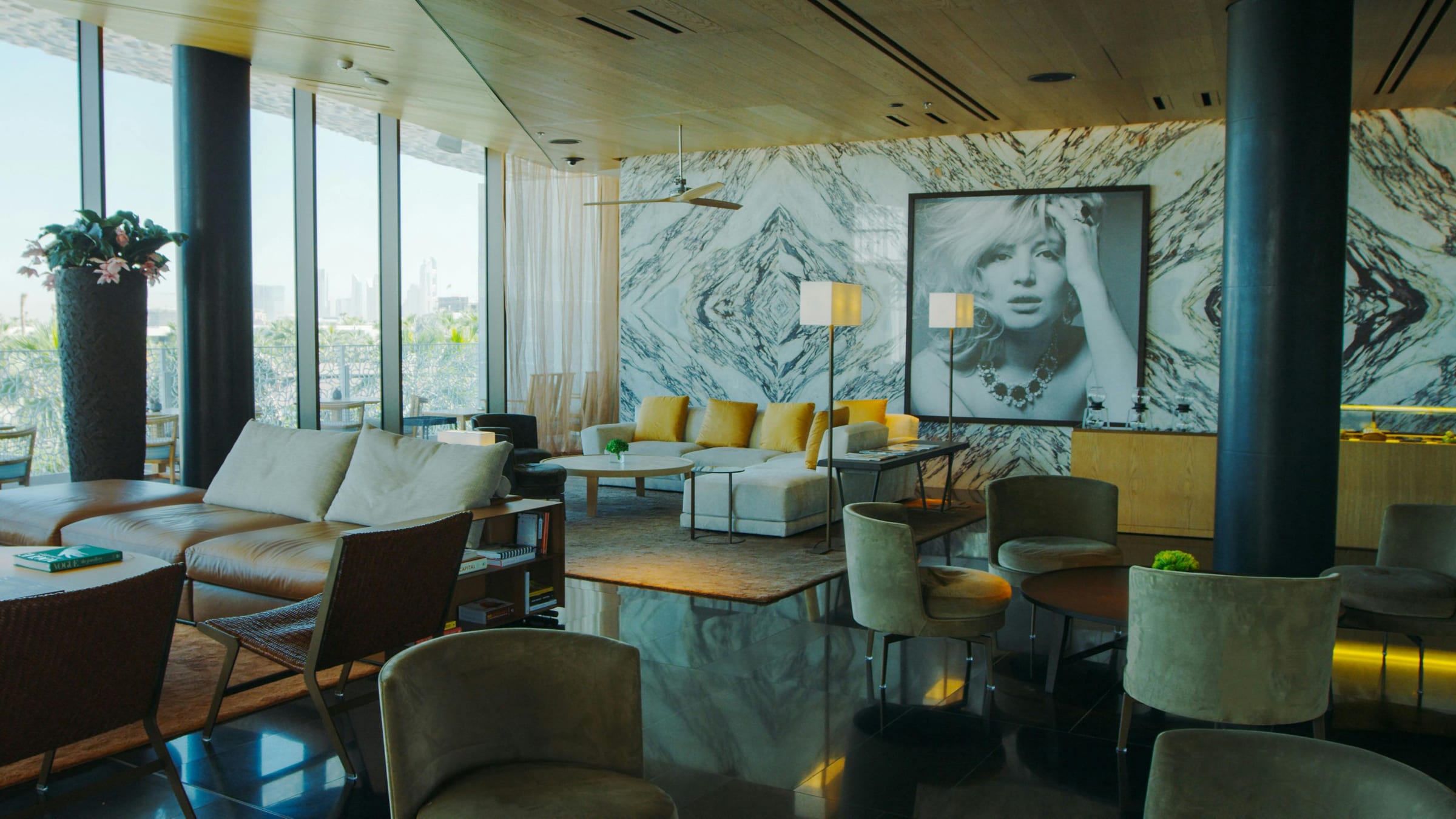 Hotel lounge with veined marble wall, framed black-and-white portrait and mustard velvet cushions
