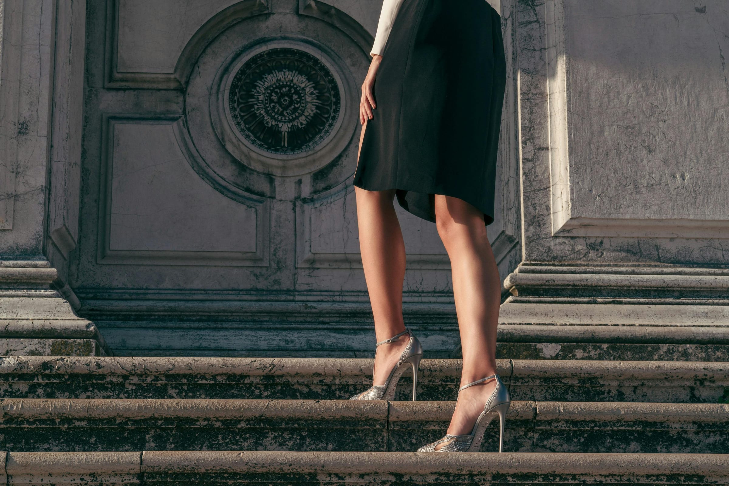 Woman in a black dress climbing Venetian marble steps in crystal René Caovilla heels