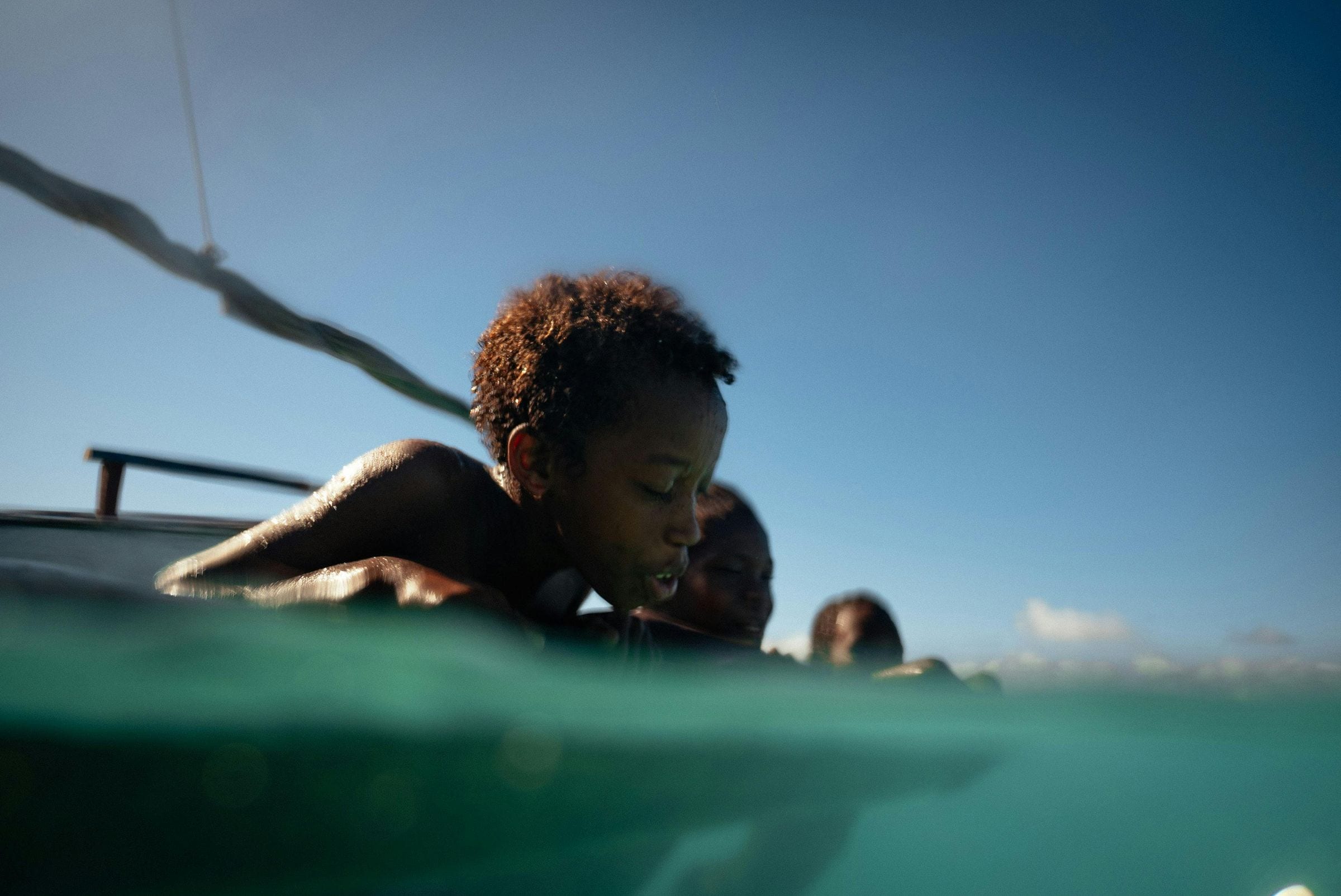 Over-under view of a young boy resting on a wooden boat above turquoise sea