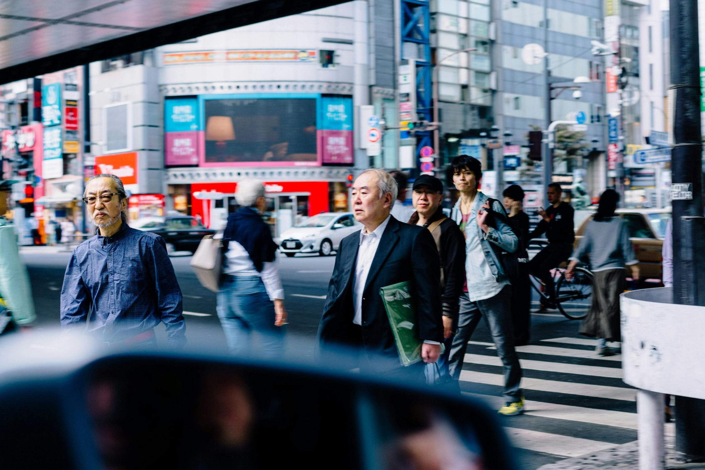 Pedestrians crossing a busy Tokyo intersection, seen through a car window