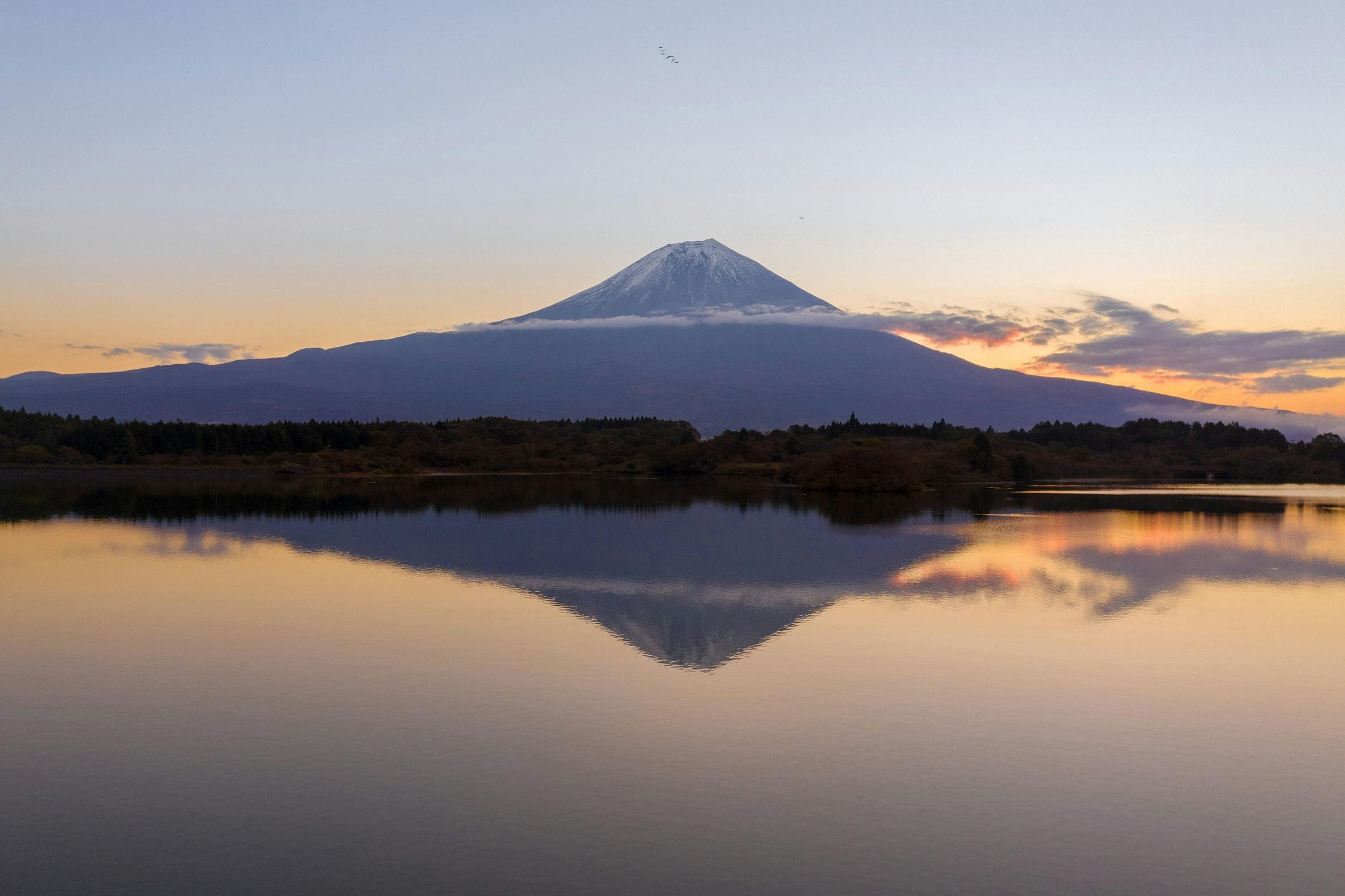 Mount Fuji mirrored in a still lake at dawn, the sky glowing orange