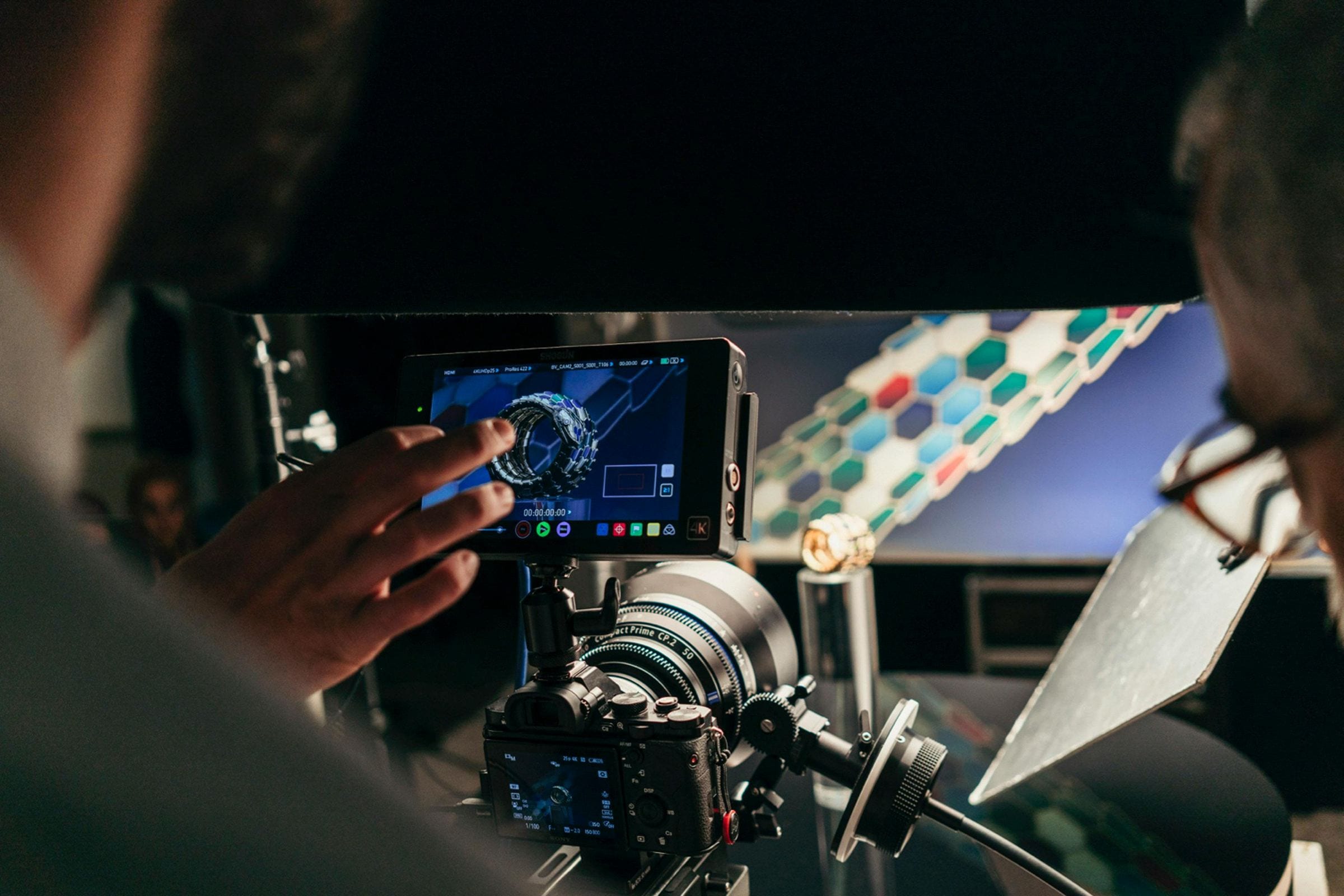 Behind the scenes at a jewelry shoot, a hand pointing to a ring on the camera monitor