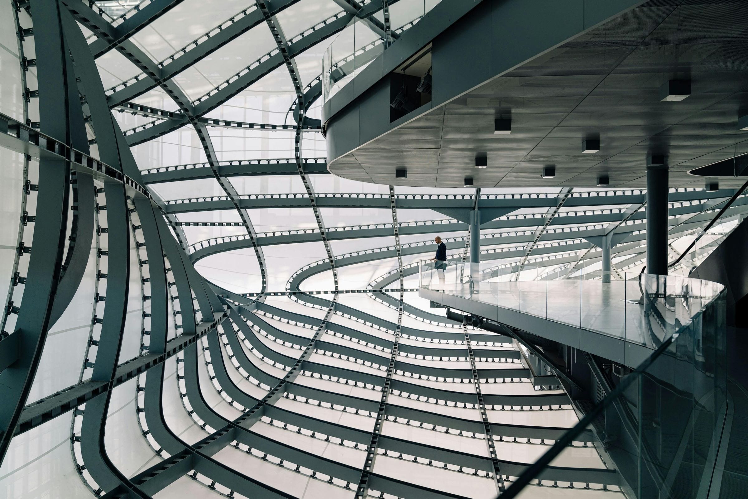 Lone suited figure on a walkway inside a soaring curved-steel Rome interior