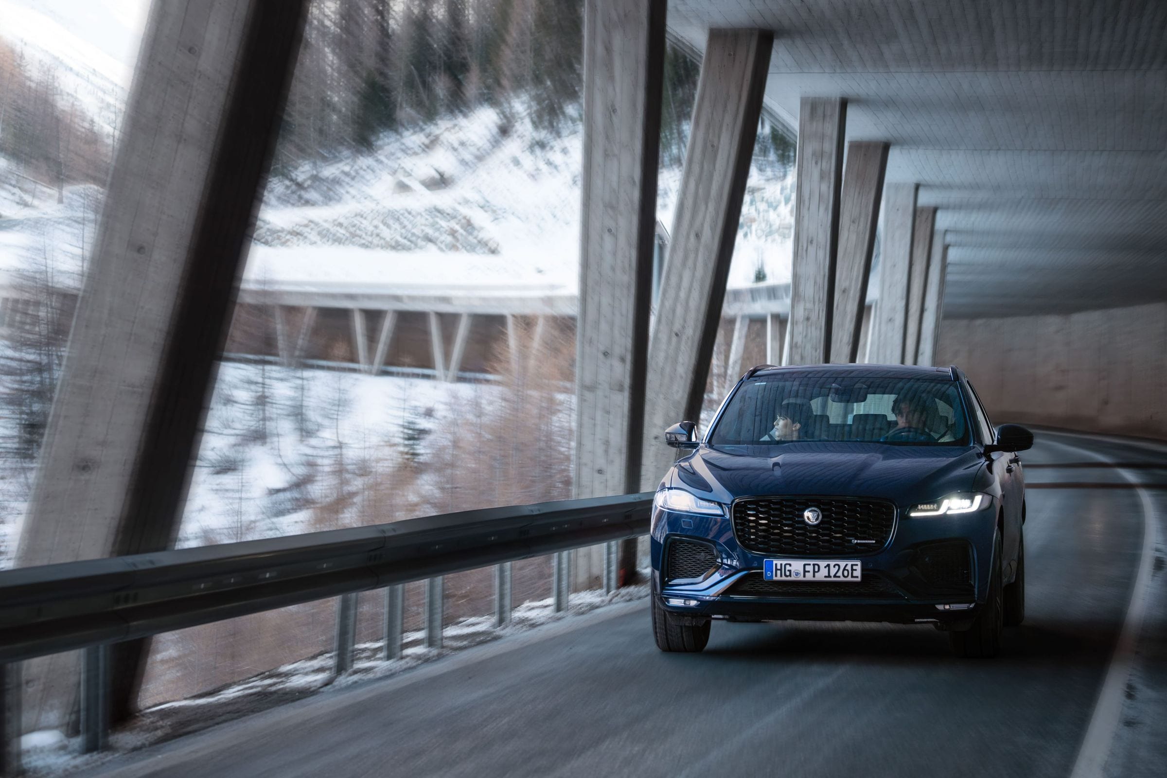A navy Jaguar F-PACE driving through an open snow gallery on an Austrian alpine pass