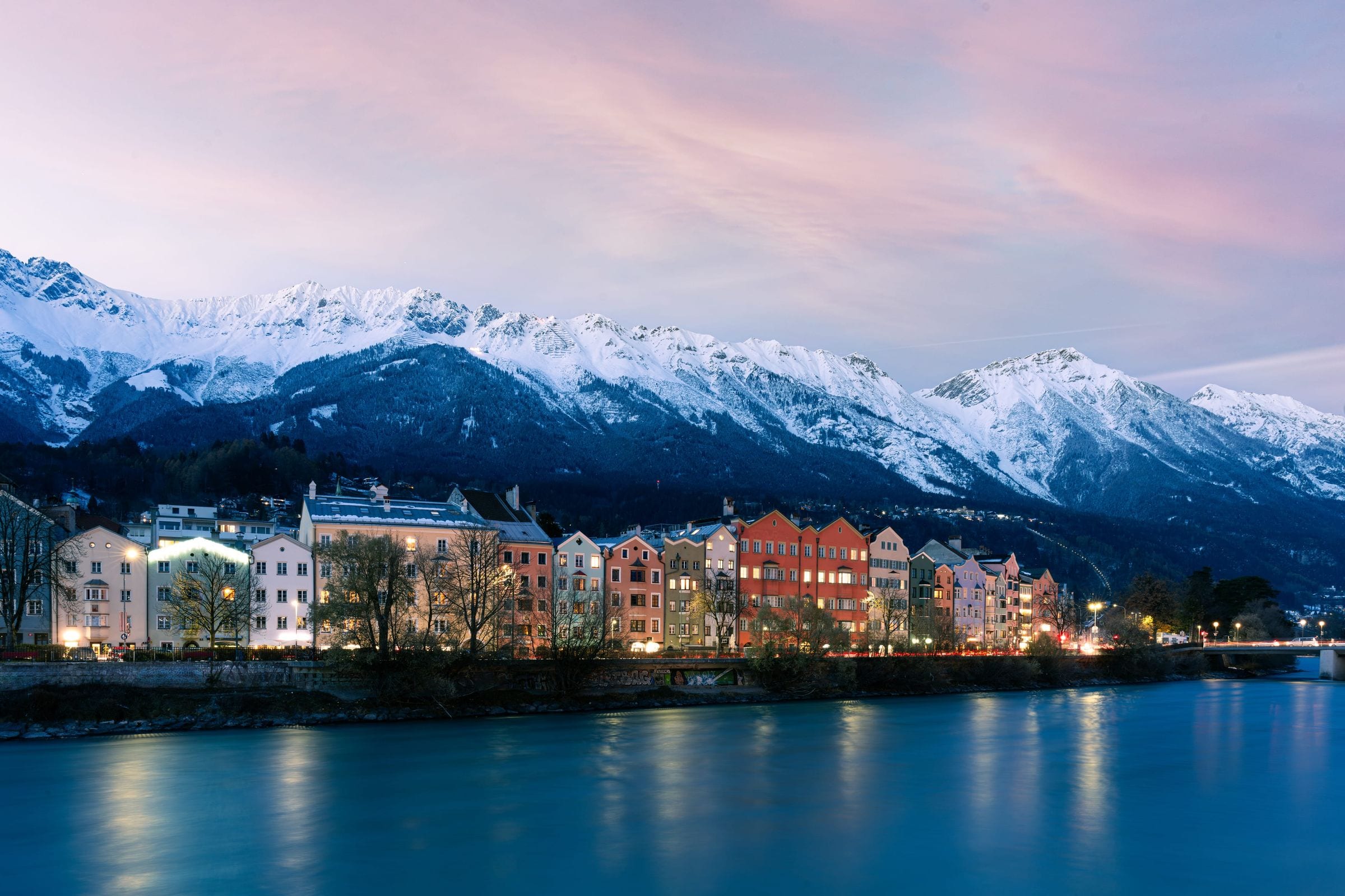 The painted houses of Innsbruck glowing at dusk along the river Inn beneath the snow-covered Nordkette range
