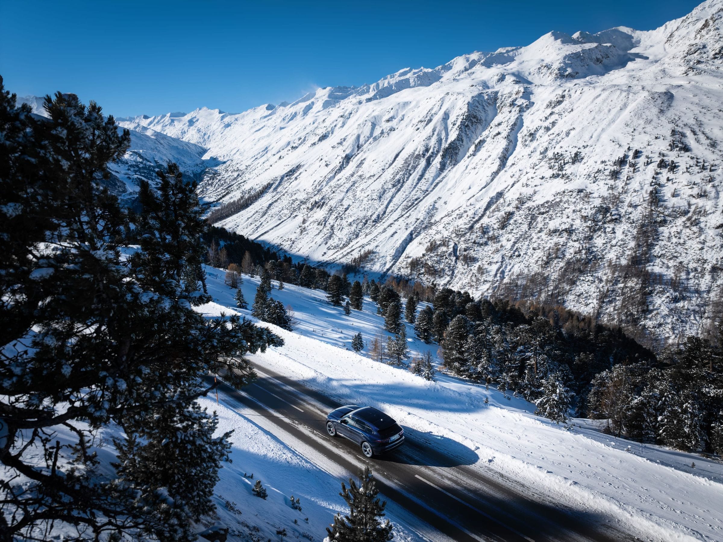 Aerial view of a navy Jaguar F-PACE on a winding snow-lined road through an Austrian alpine valley