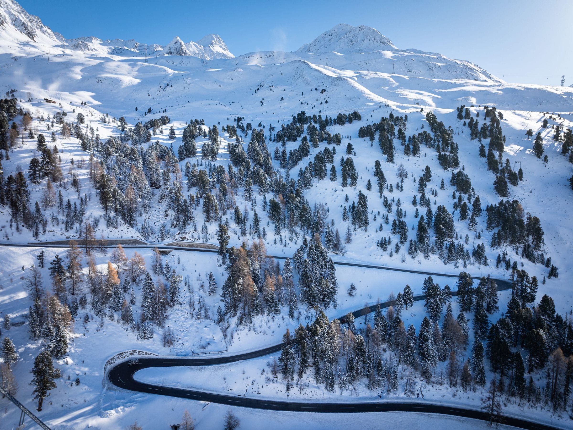 Aerial view of a serpentine mountain road through snow-covered larch forest in the Austrian Tirol
