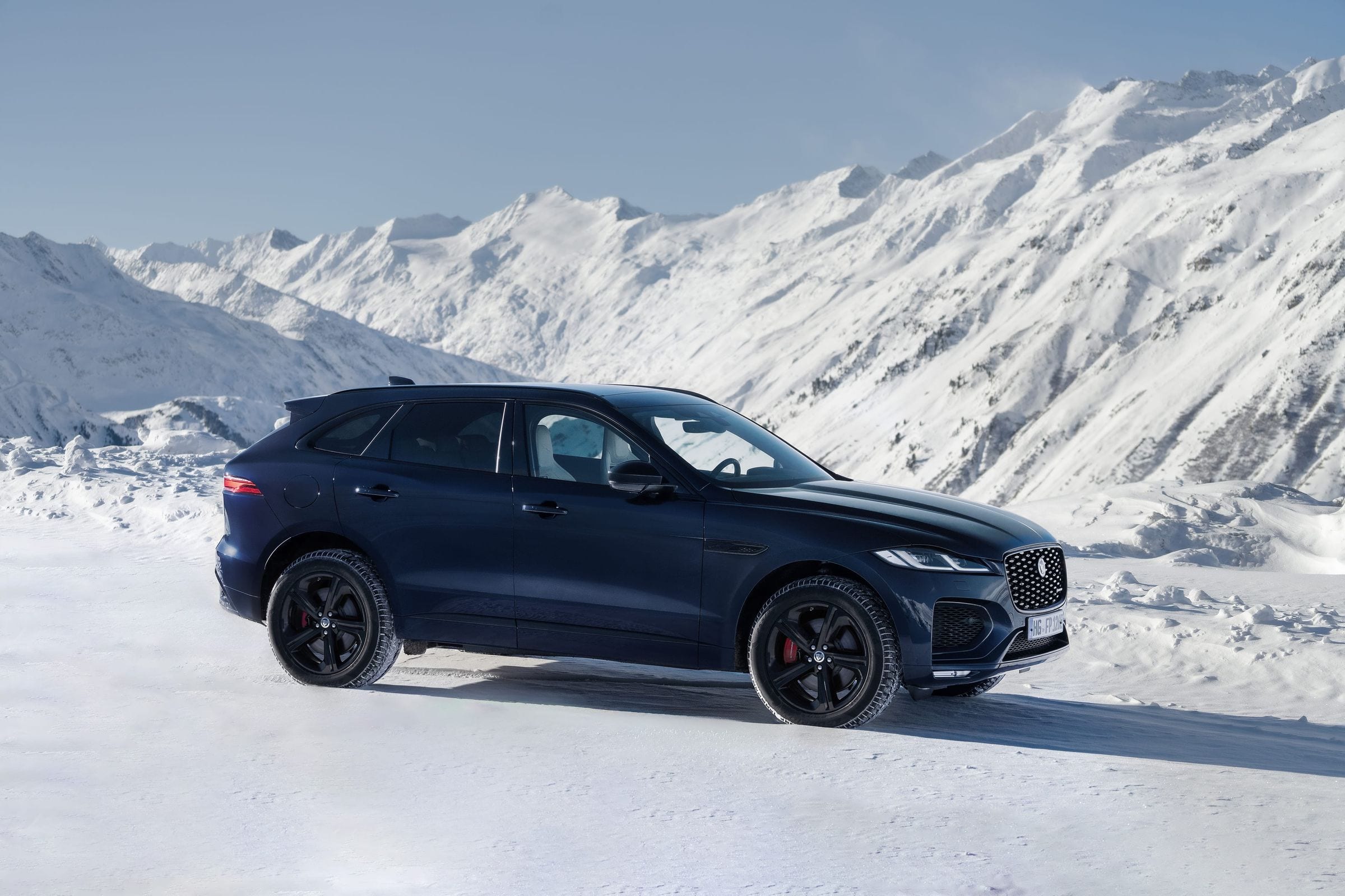 A navy Jaguar F-PACE parked on snow with a wide panorama of the Austrian Alps behind it