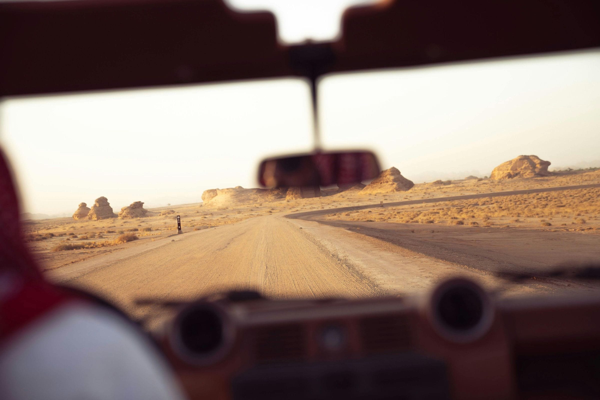 View through a vehicle windshield onto a golden desert track at sunset