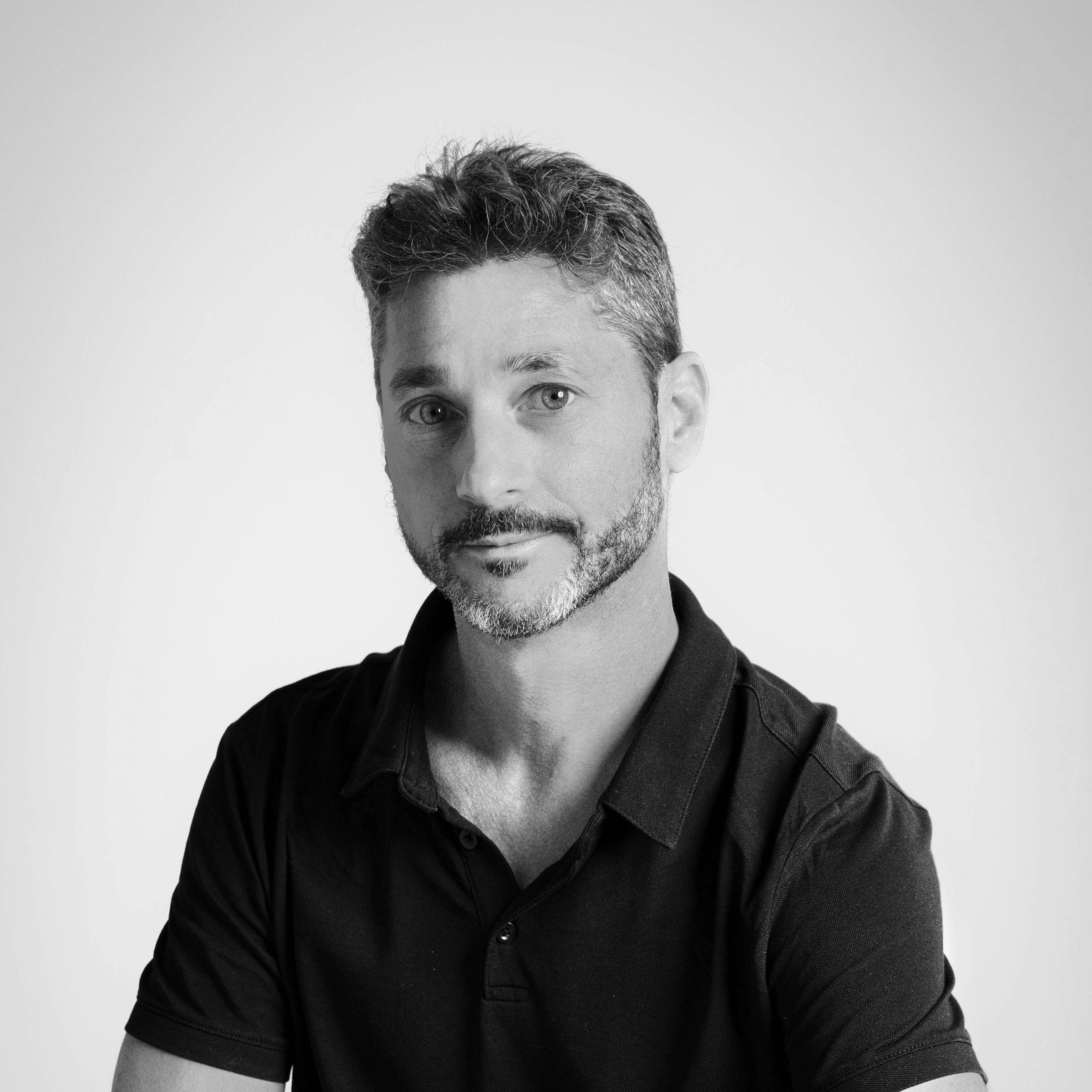 Black-and-white studio portrait of a bearded man in a dark polo shirt