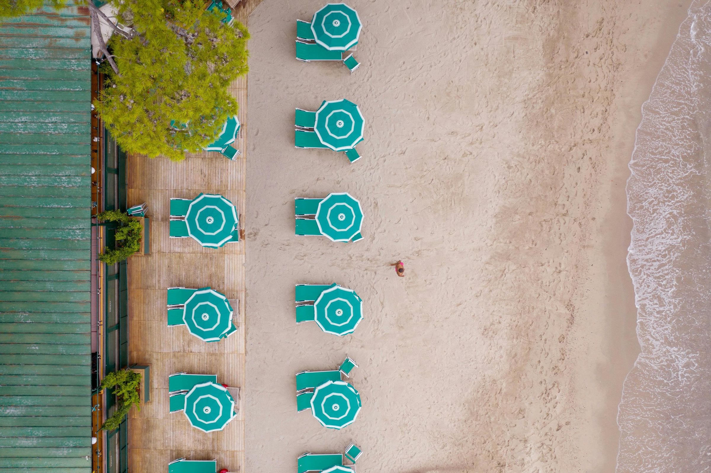 Overhead view of green striped beach umbrellas and loungers on golden Portofino sand