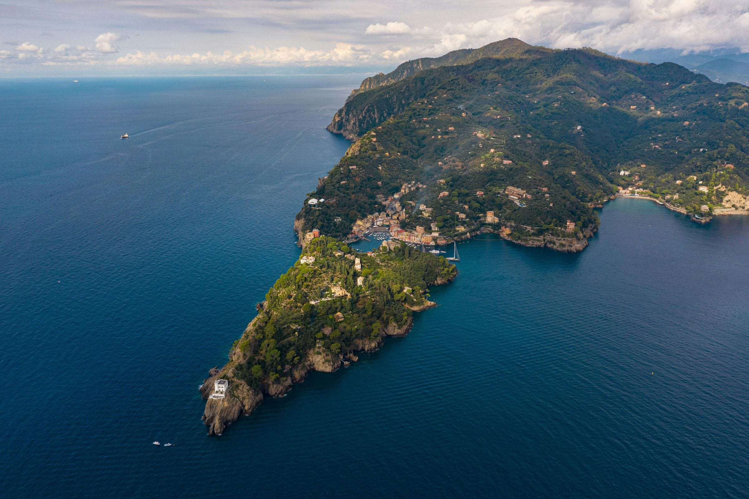 Aerial of Portofino harbor village nestled in its green headland above deep blue sea