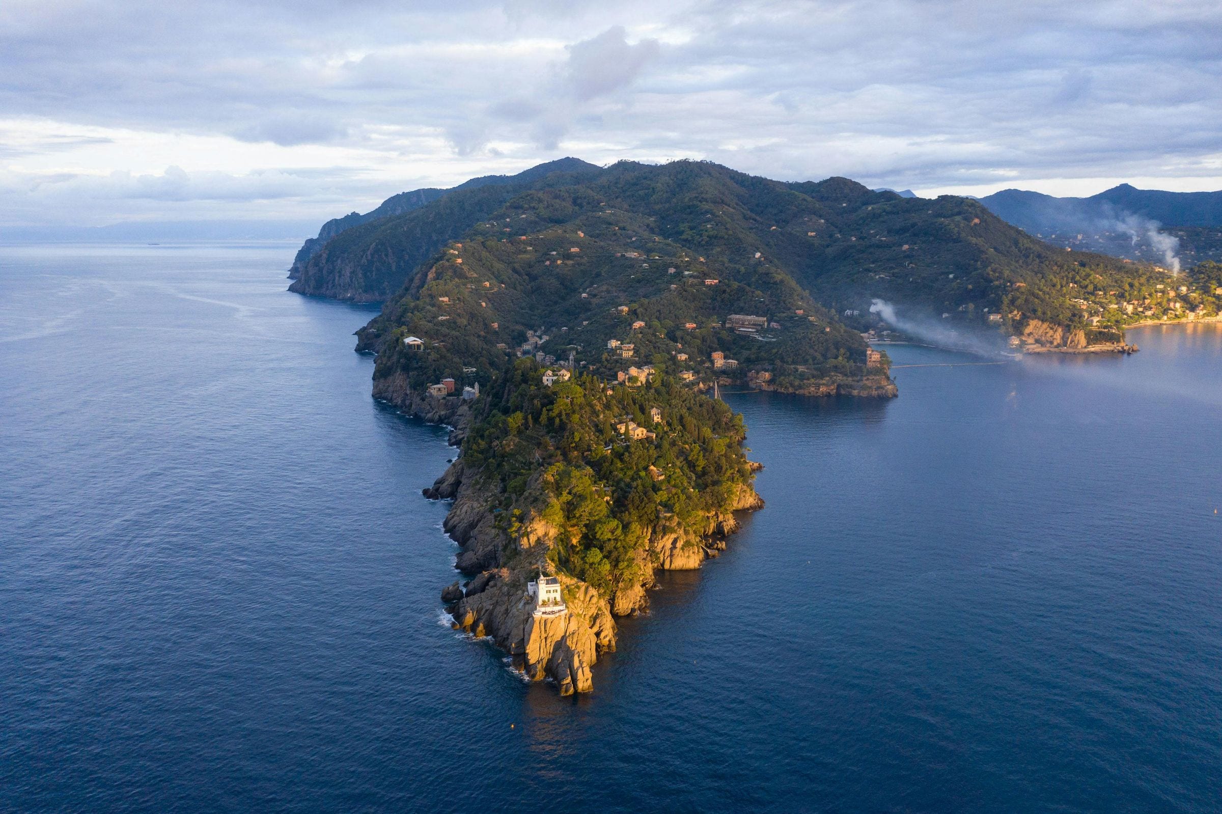 Golden-hour aerial of the wooded Portofino promontory reaching into the Ligurian Sea