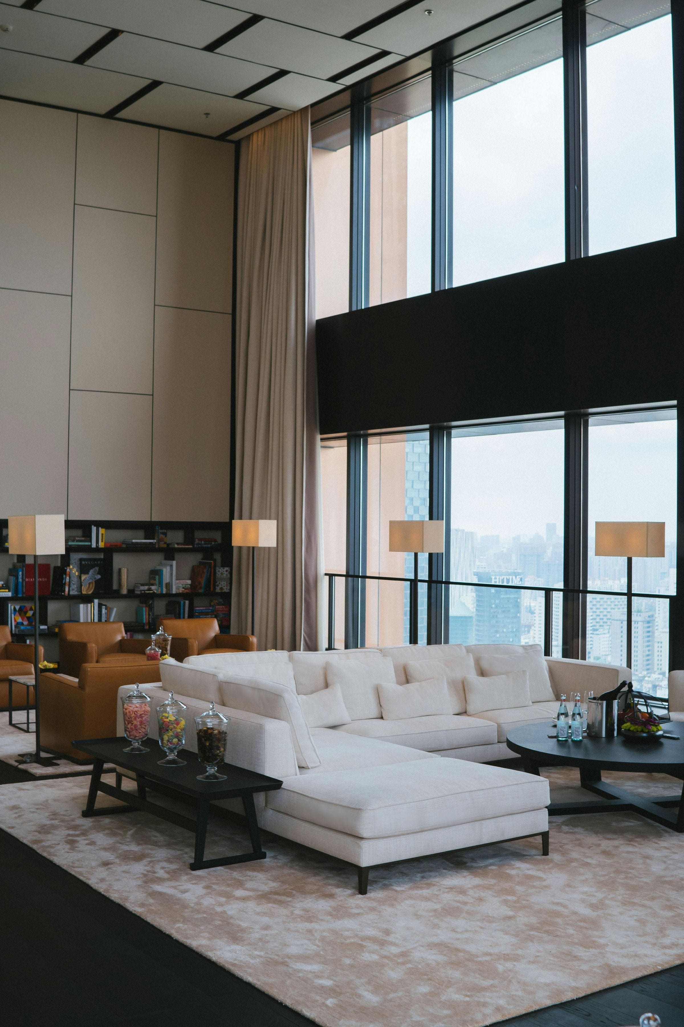 Double-height suite lounge with cream sectional and candy jars, city skyline through tall windows