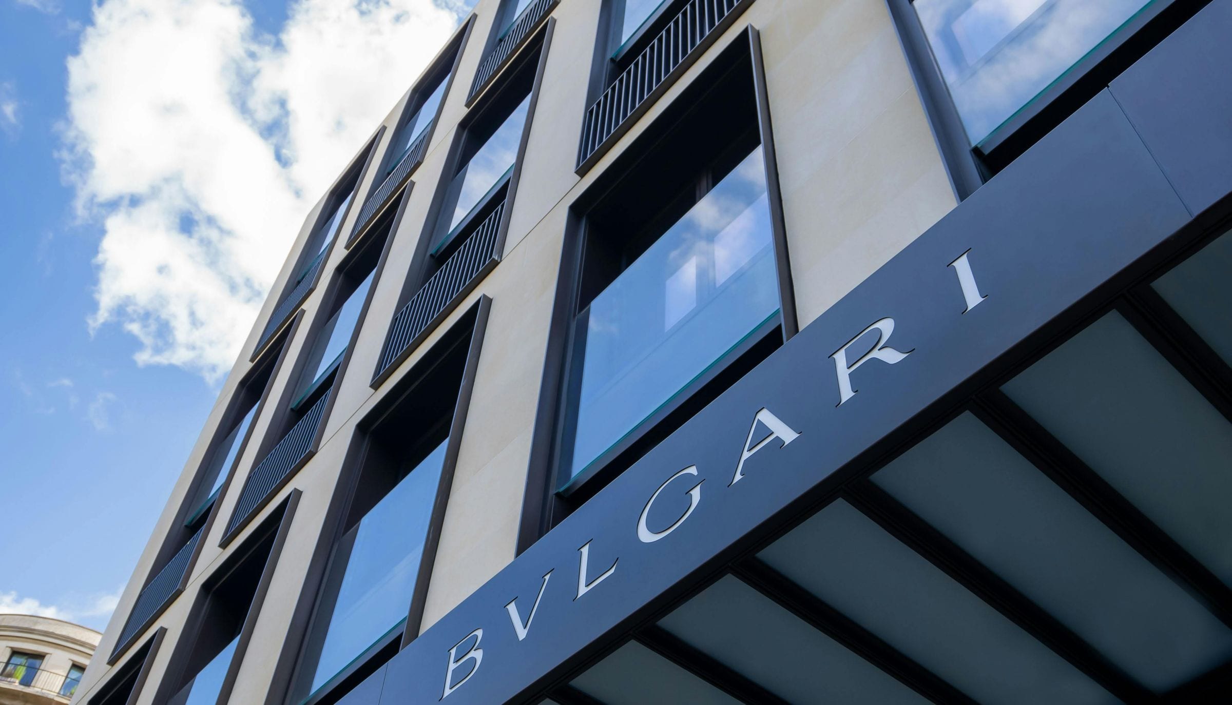 Looking up at the Bvlgari nameplate on a stone-and-glass hotel facade against blue sky
