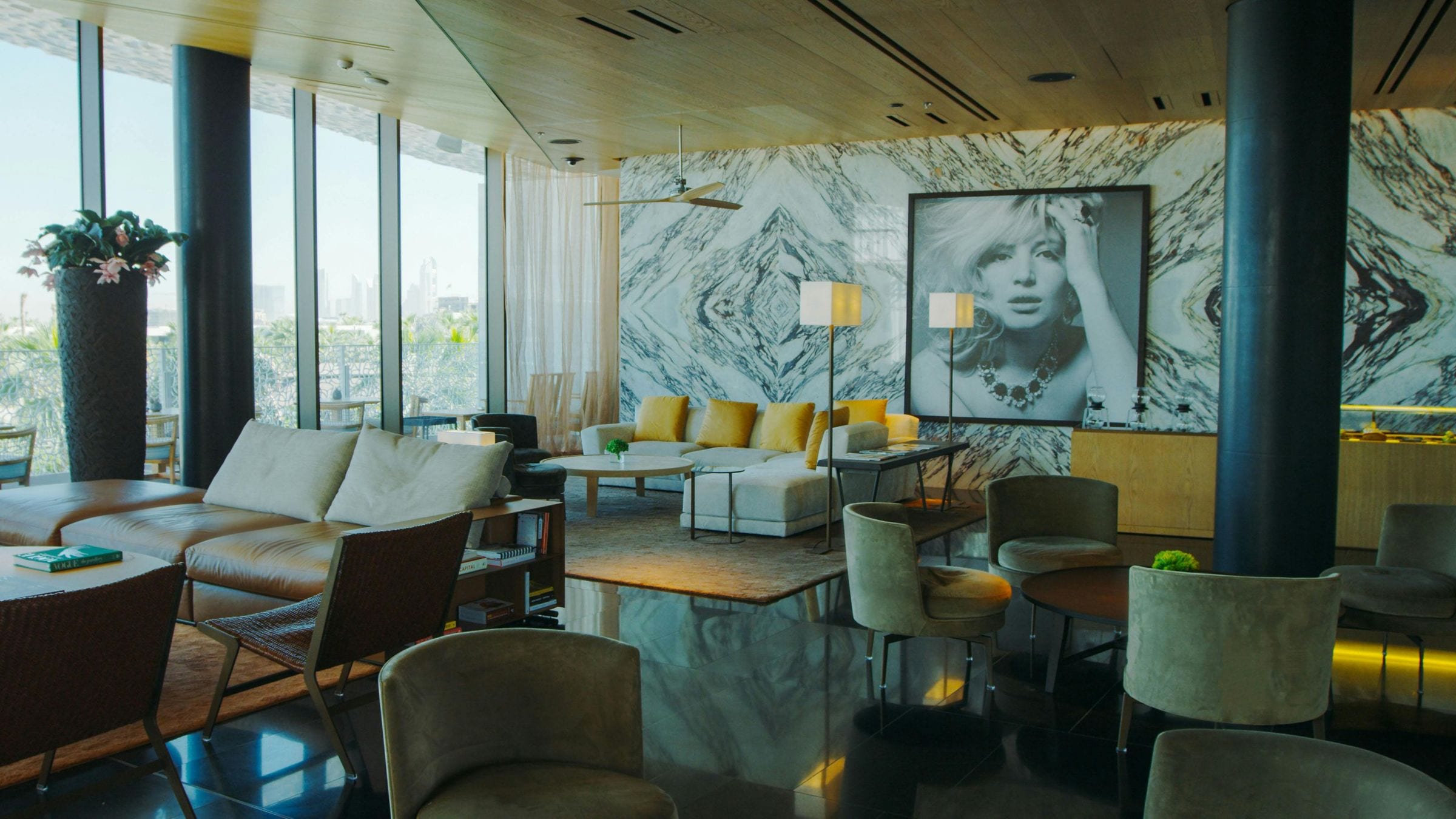 Hotel lounge with veined marble wall, framed black-and-white portrait and mustard velvet cushions