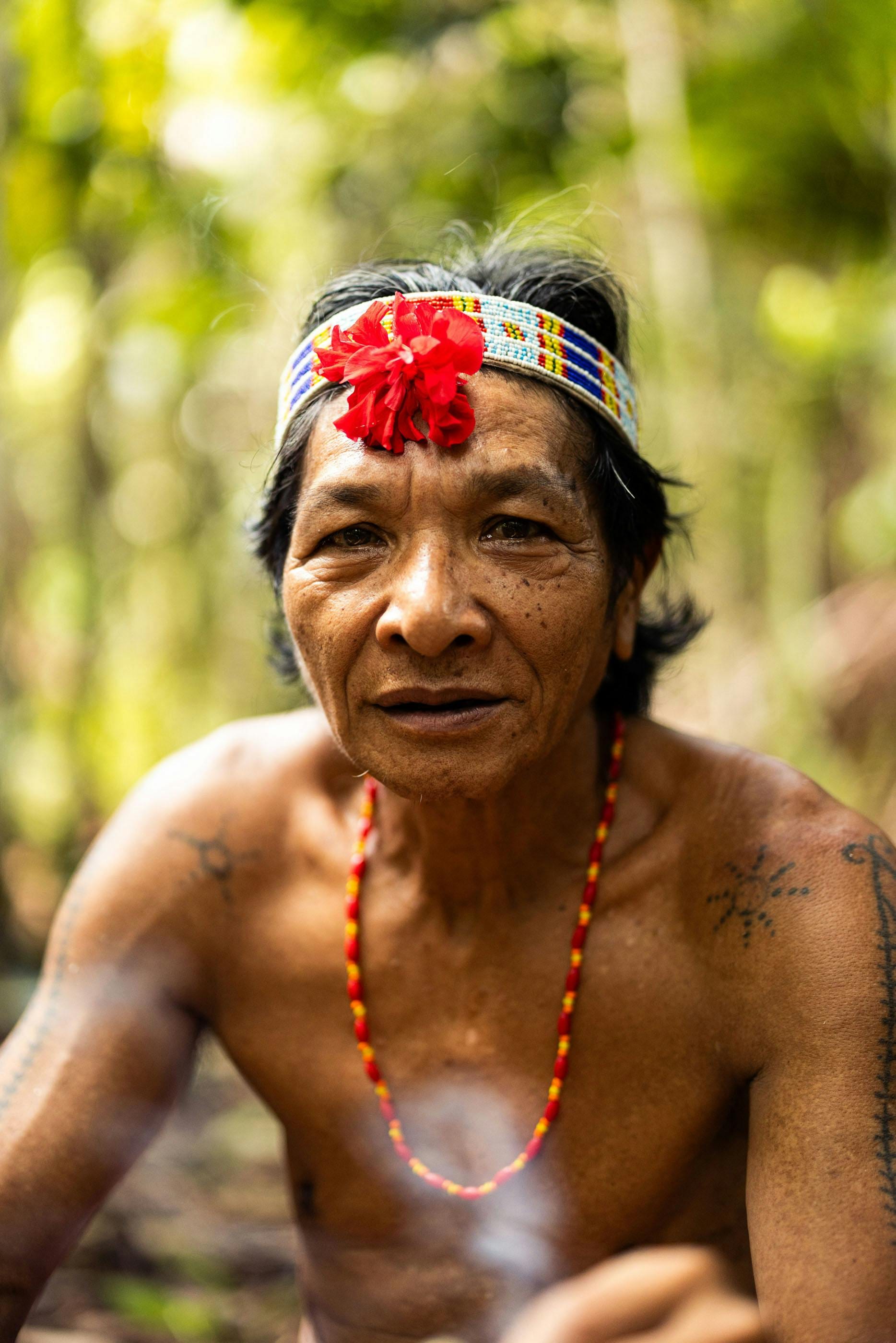 Portrait of a tattooed Mentawai elder in a beaded headband and red flower