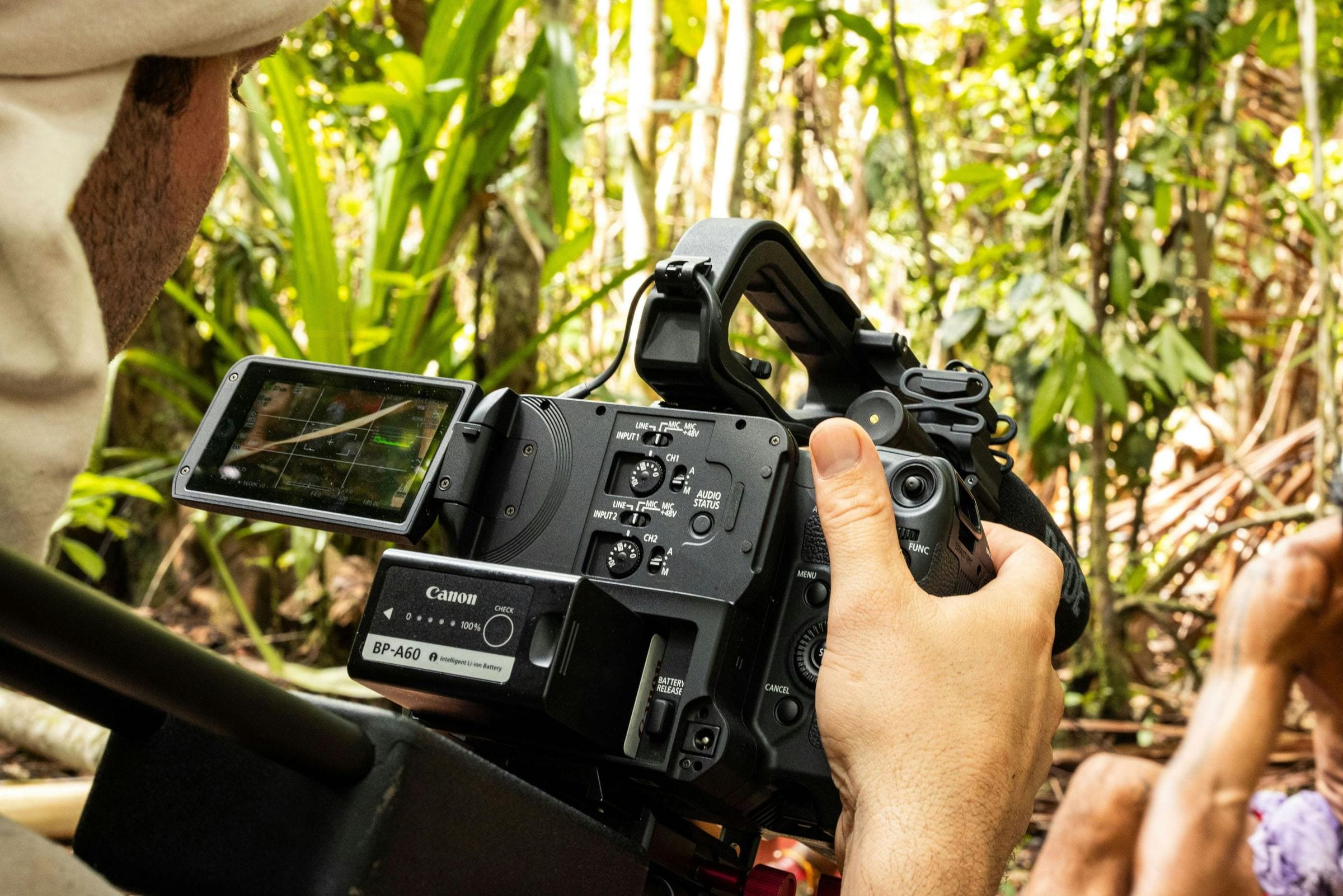 Hands operating a Canon cinema camera while filming in the jungle