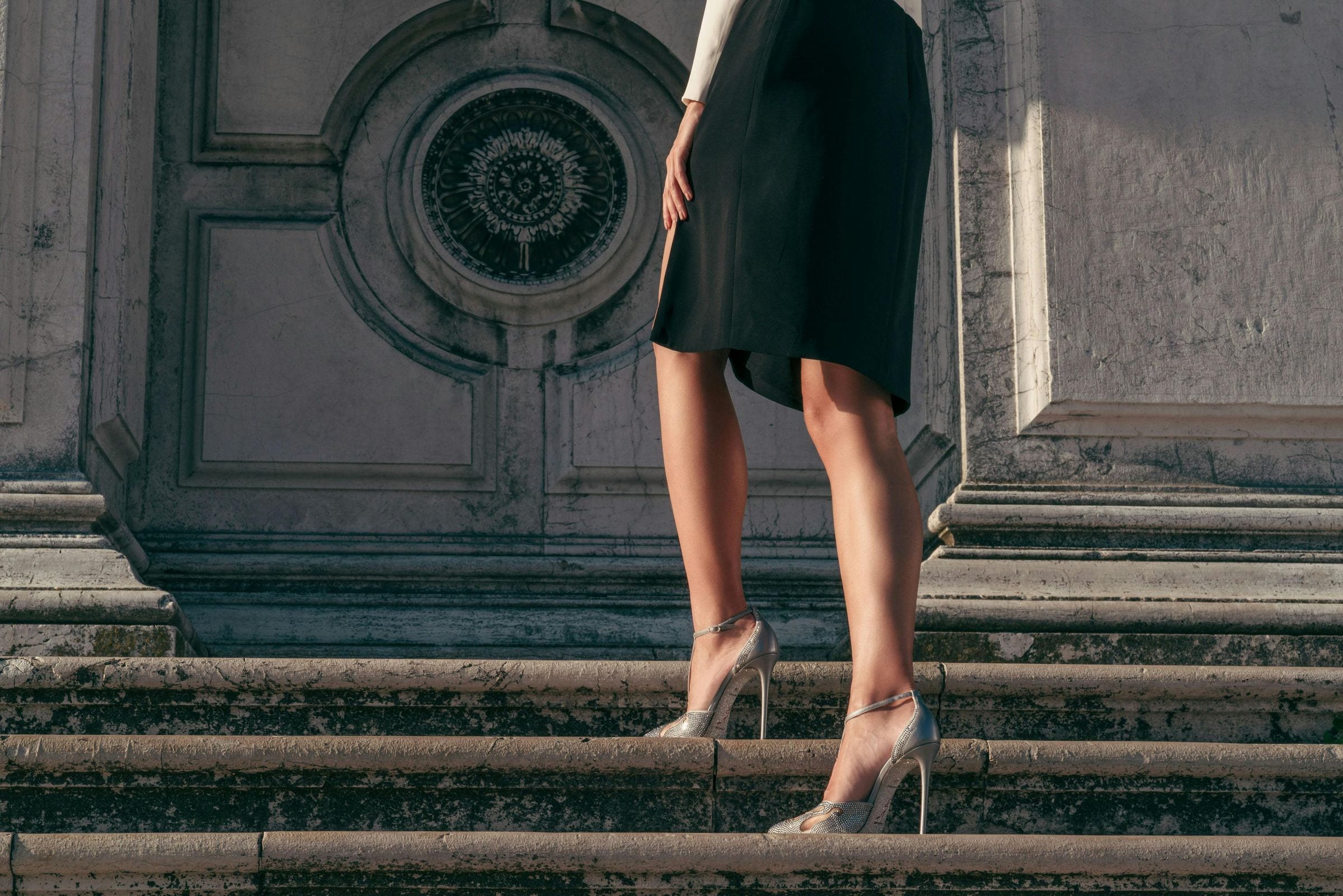 Woman in a black dress climbing Venetian marble steps in crystal René Caovilla heels