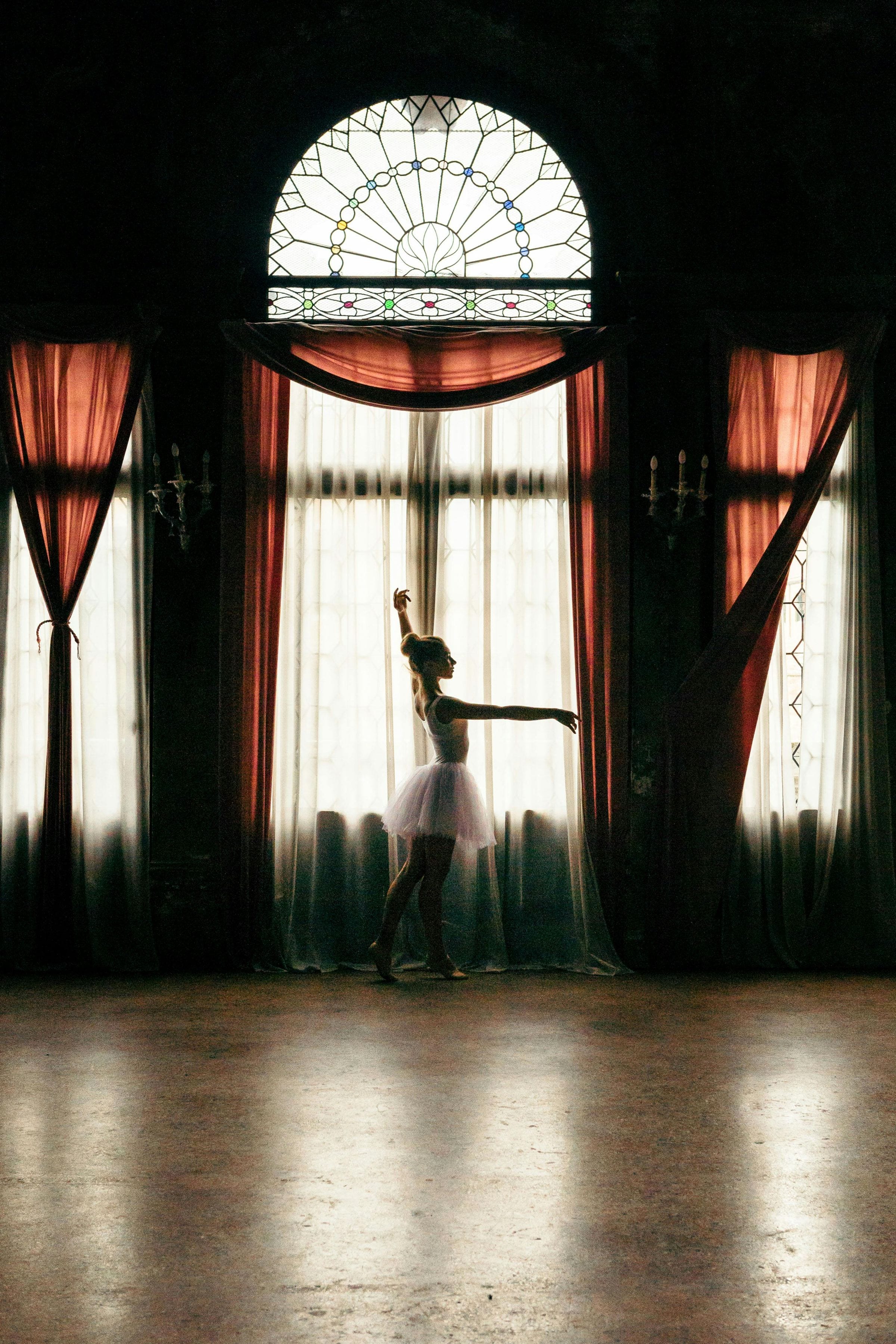 Ballerina in a white tutu silhouetted against a stained-glass window in a Venetian palazzo