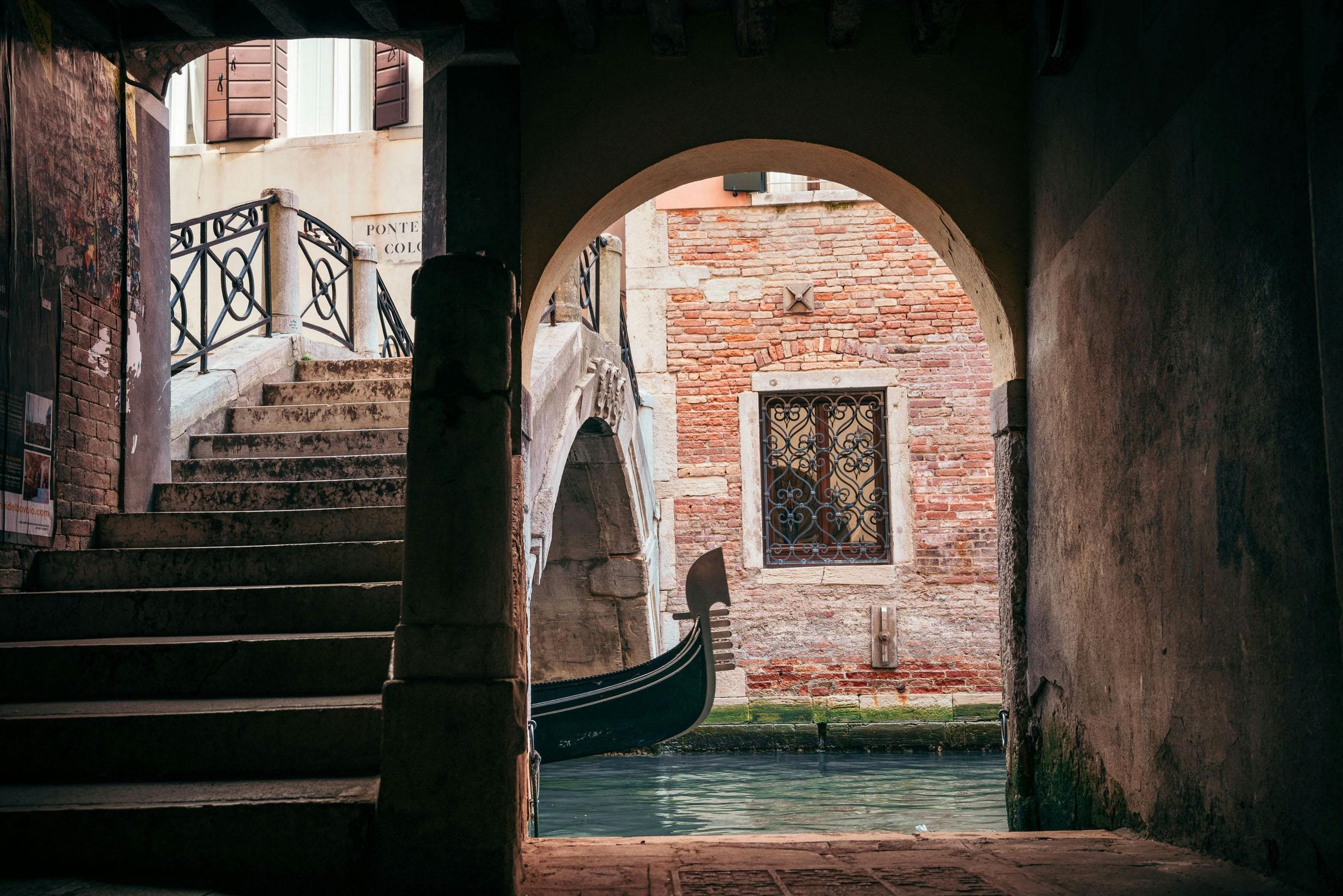 Moored gondola and stone bridge glimpsed through a shadowed Venetian archway