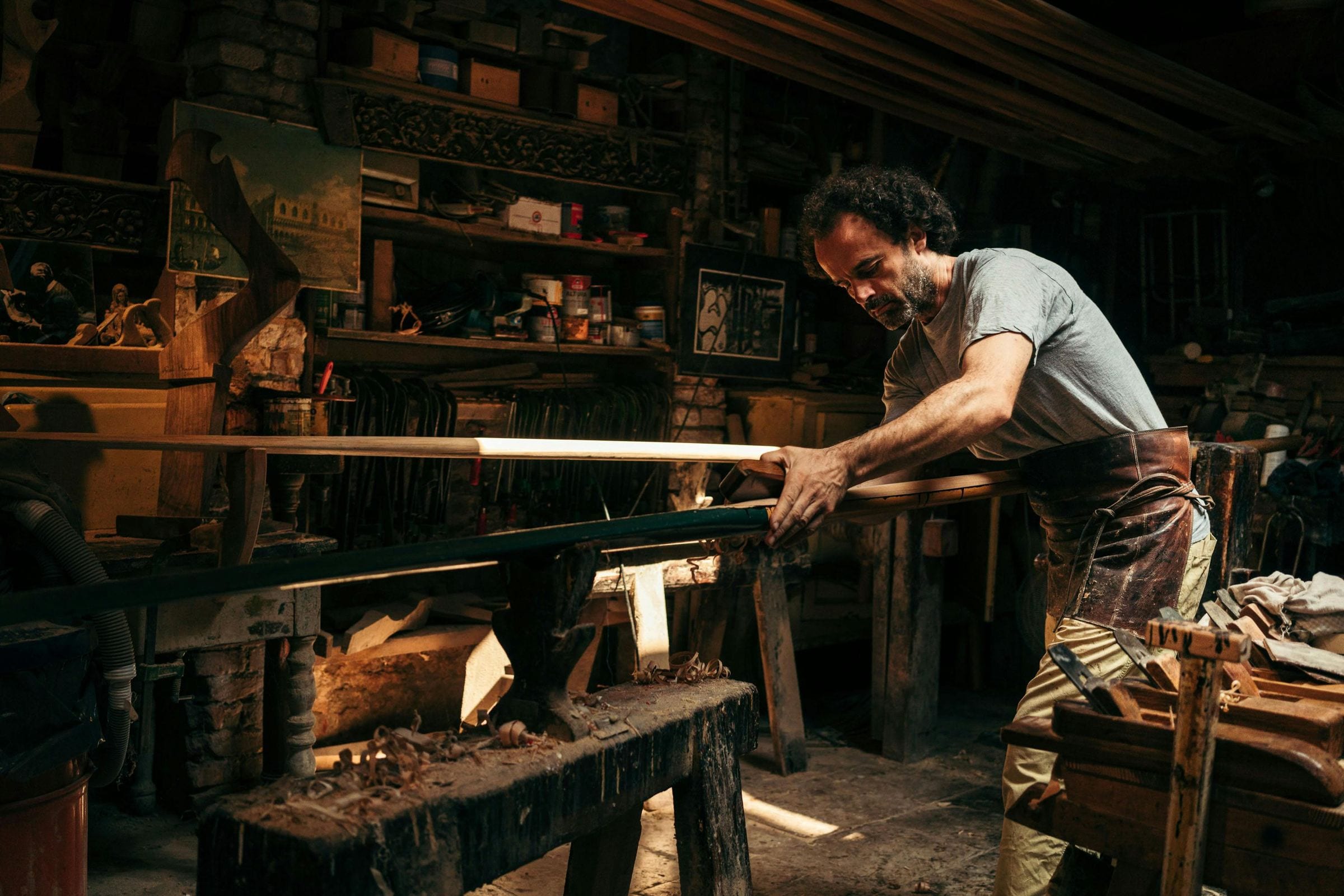 Craftsman planing a gondola oar in a dim Venetian workshop