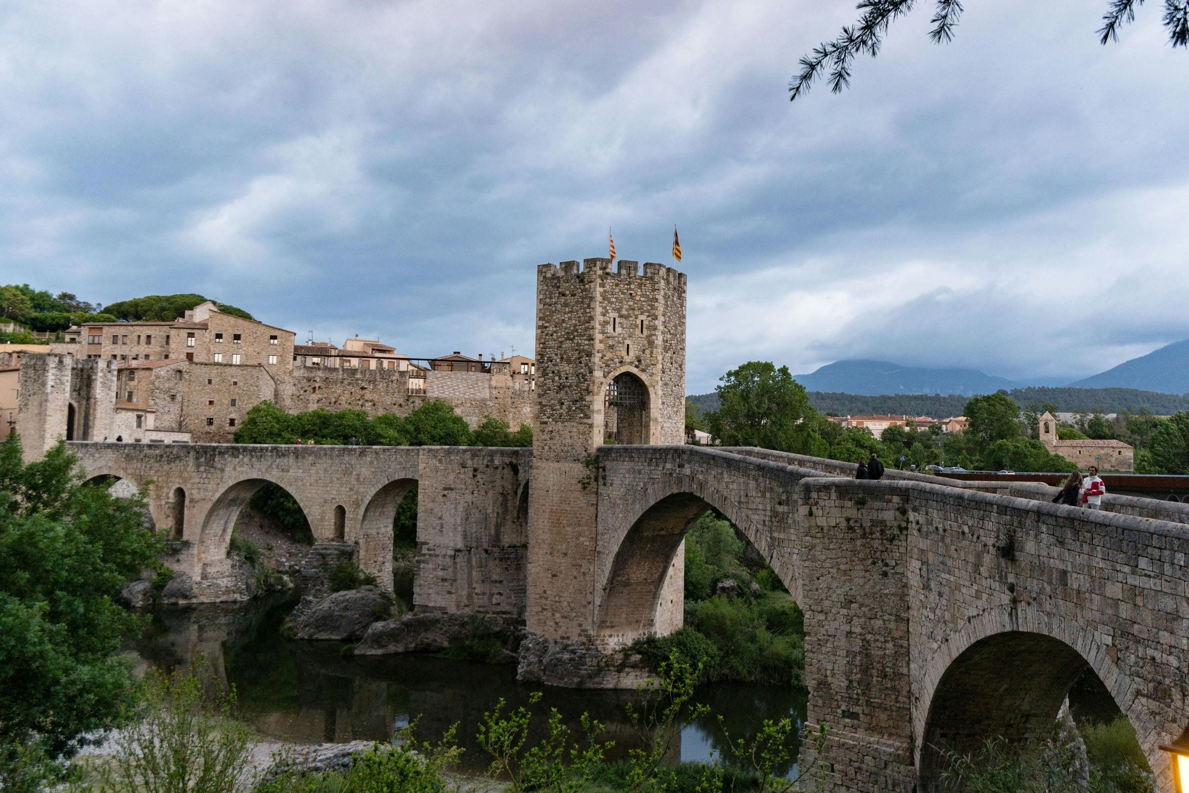 Medieval fortified bridge and tower over a river flying Catalan flags, Besalú