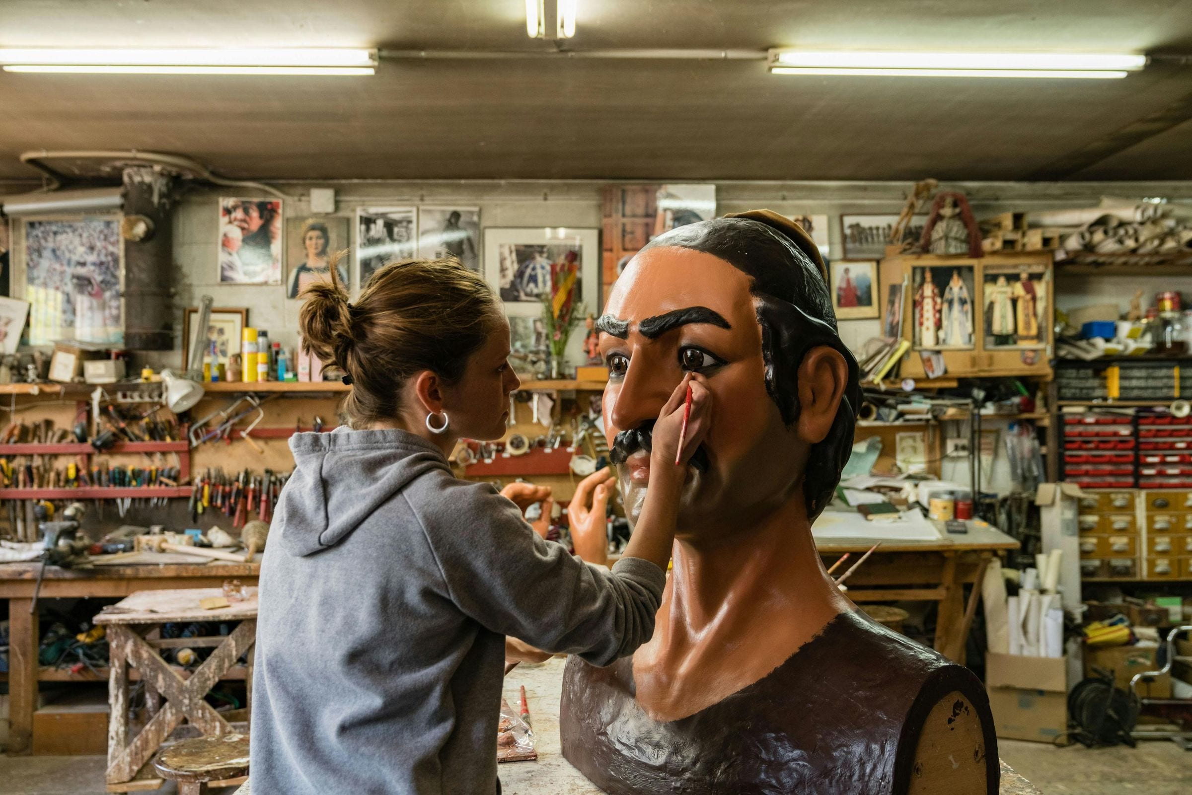 Young woman paints the eye of a giant carnival figure's head in a workshop