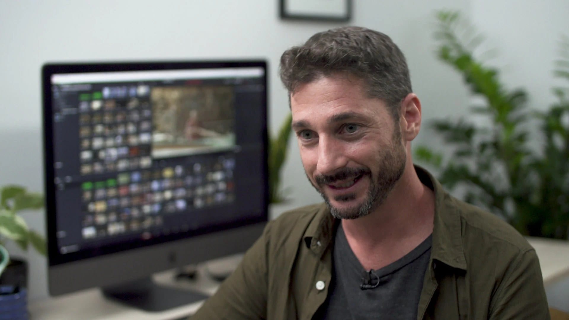 Oliver Astrologo at his editing desk, a DaVinci Resolve timeline full of clips on the screen behind him