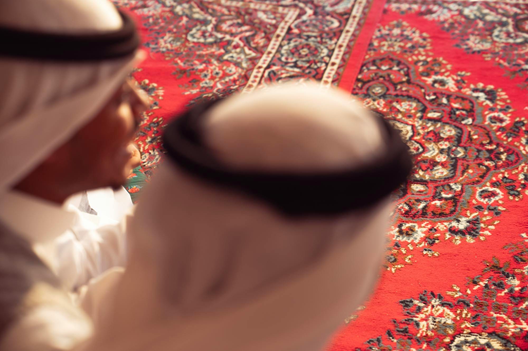 Two men in traditional Saudi headdress seated over a red patterned carpet