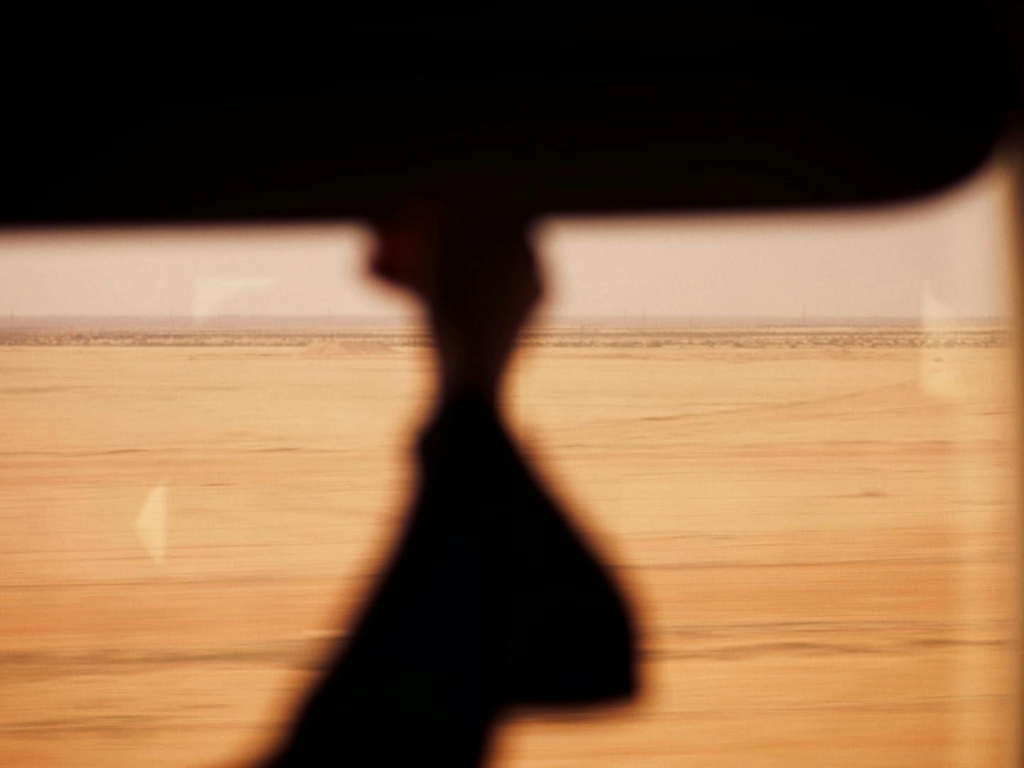 Silhouetted traveler seen through a train window against a passing desert plain