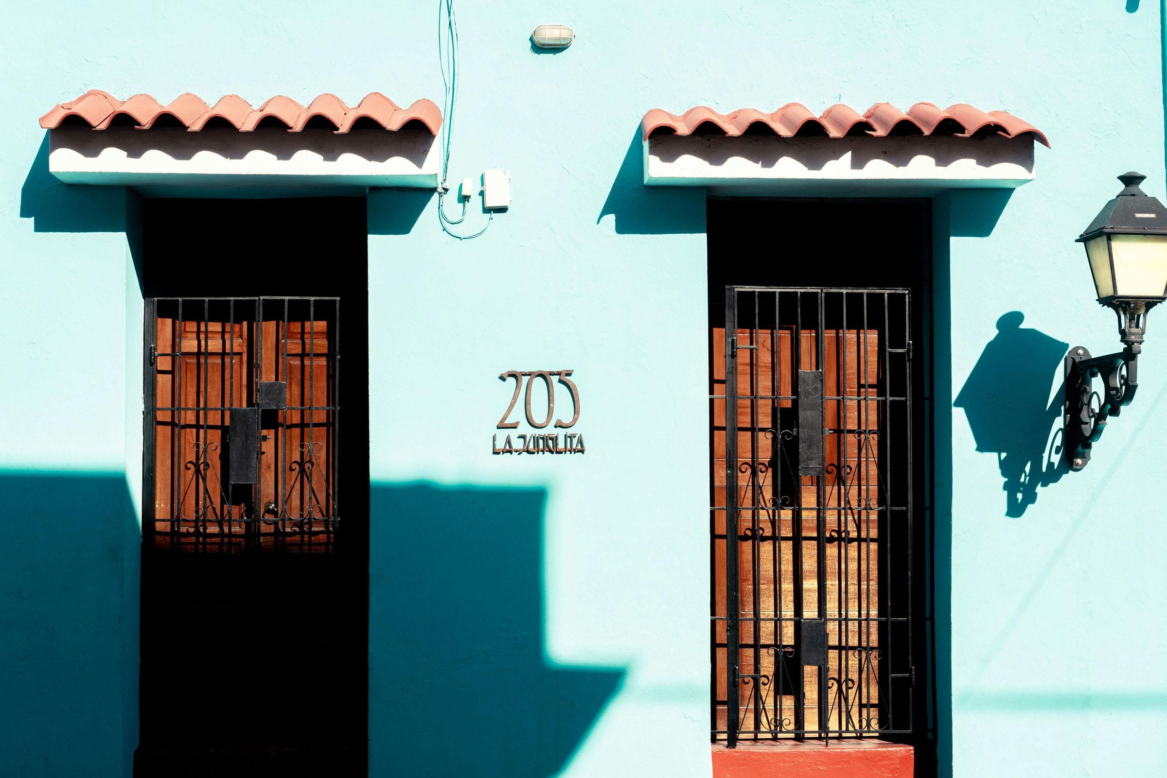 Turquoise colonial facade with barred wooden doors and a wrought-iron street lantern