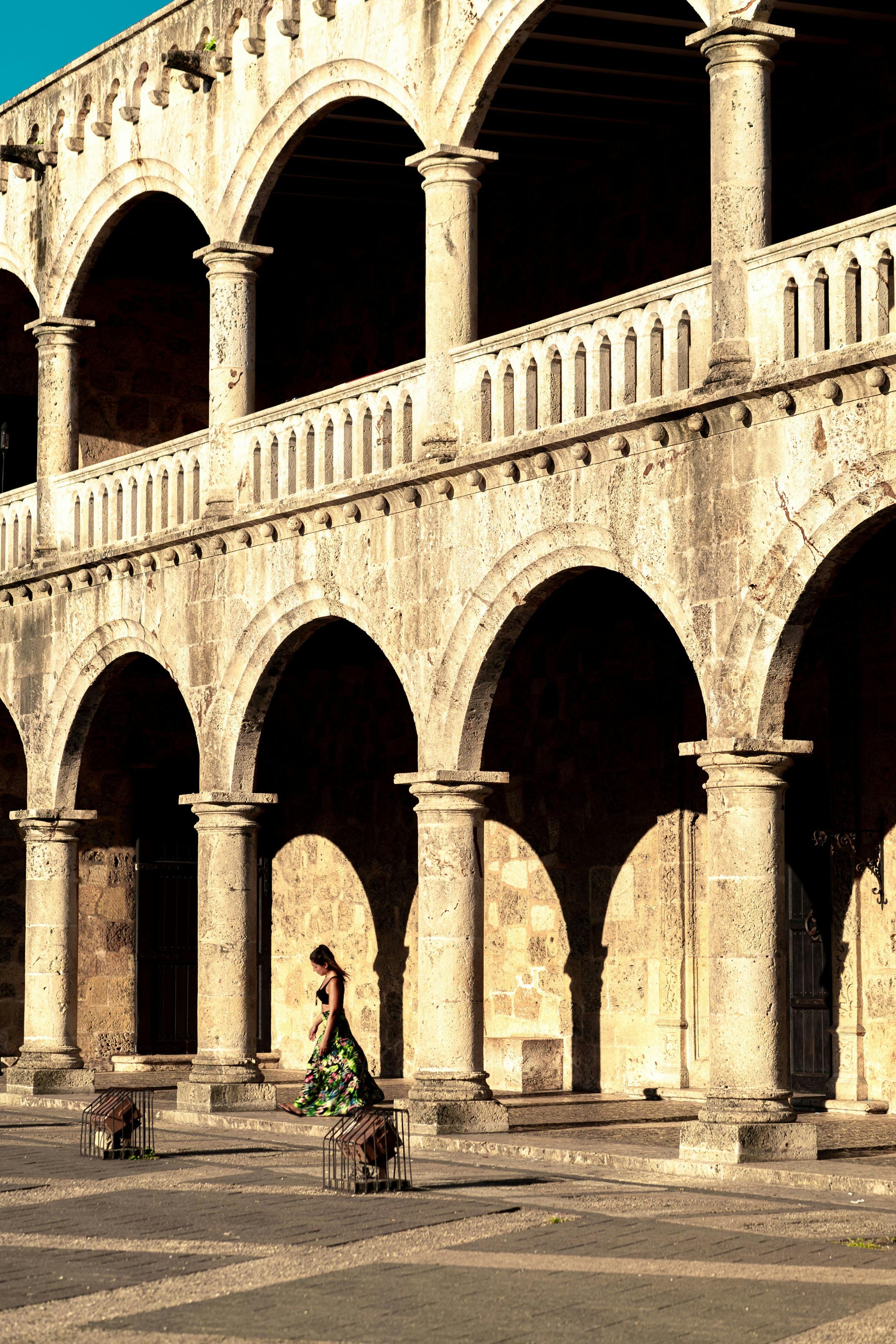 Woman in a floral dress walking beneath colonial stone arcades, Santo Domingo
