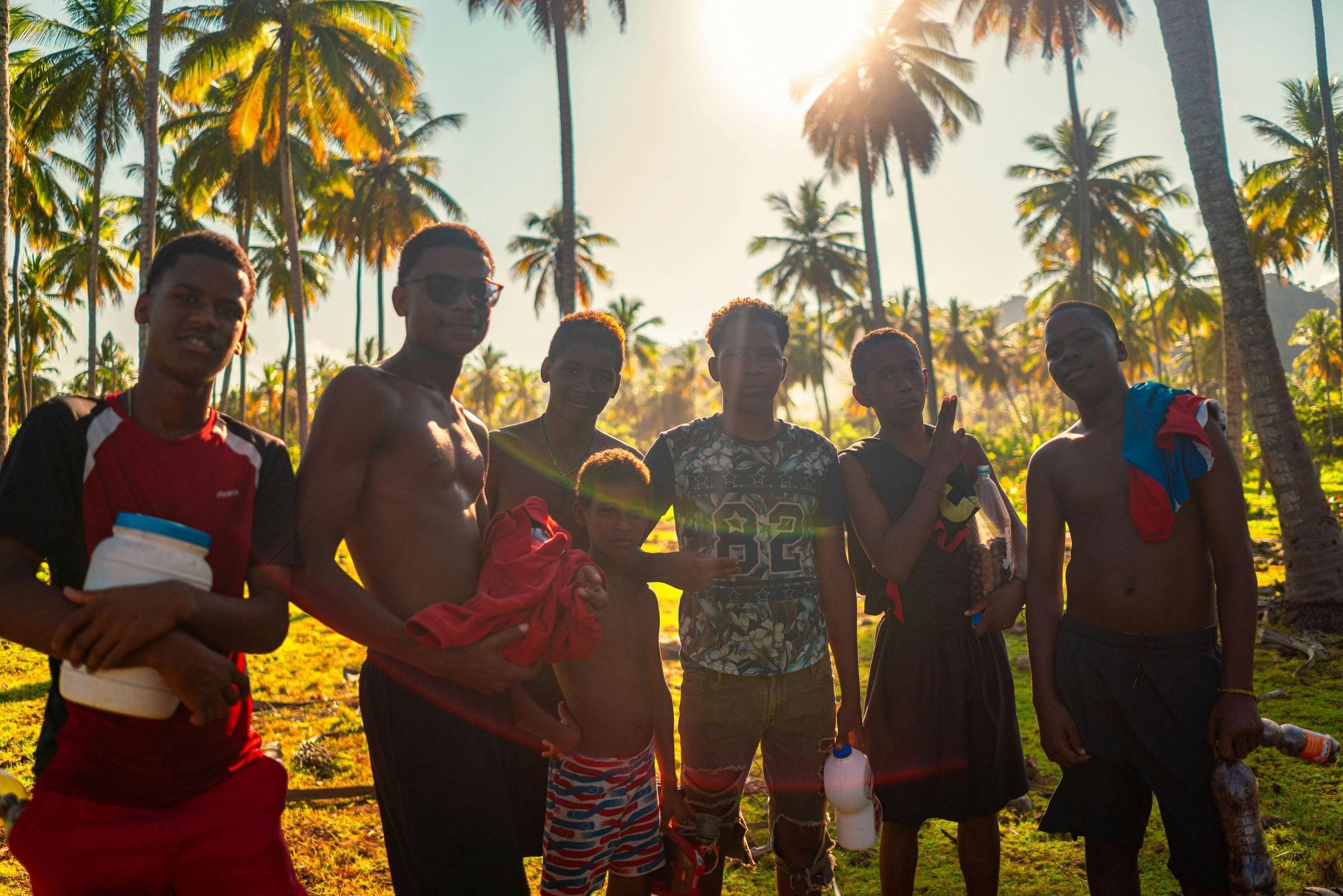 Group of local boys posing under backlit palms at sunset, one flashing a peace sign