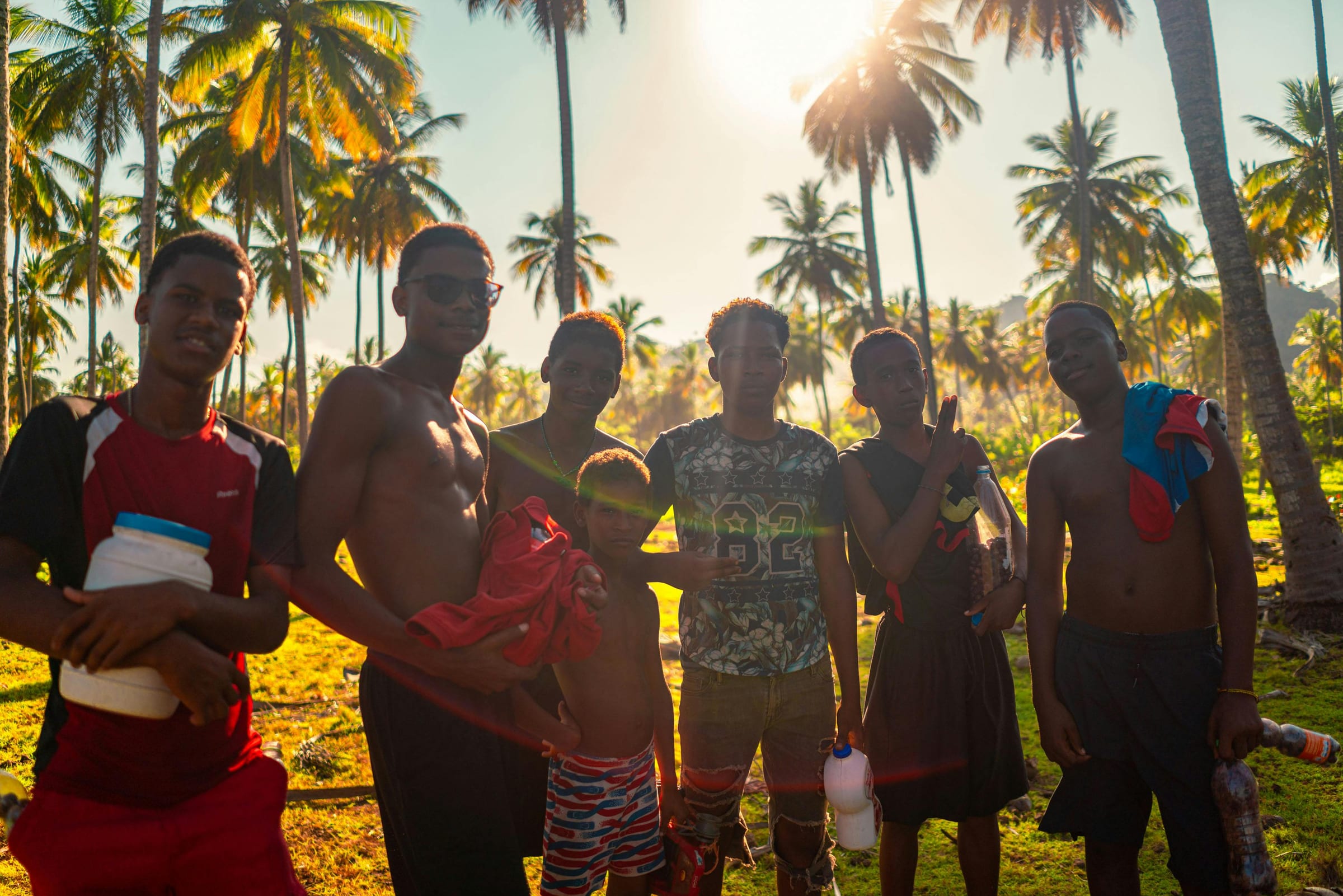 Group of local boys posing under backlit palms at sunset, one flashing a peace sign