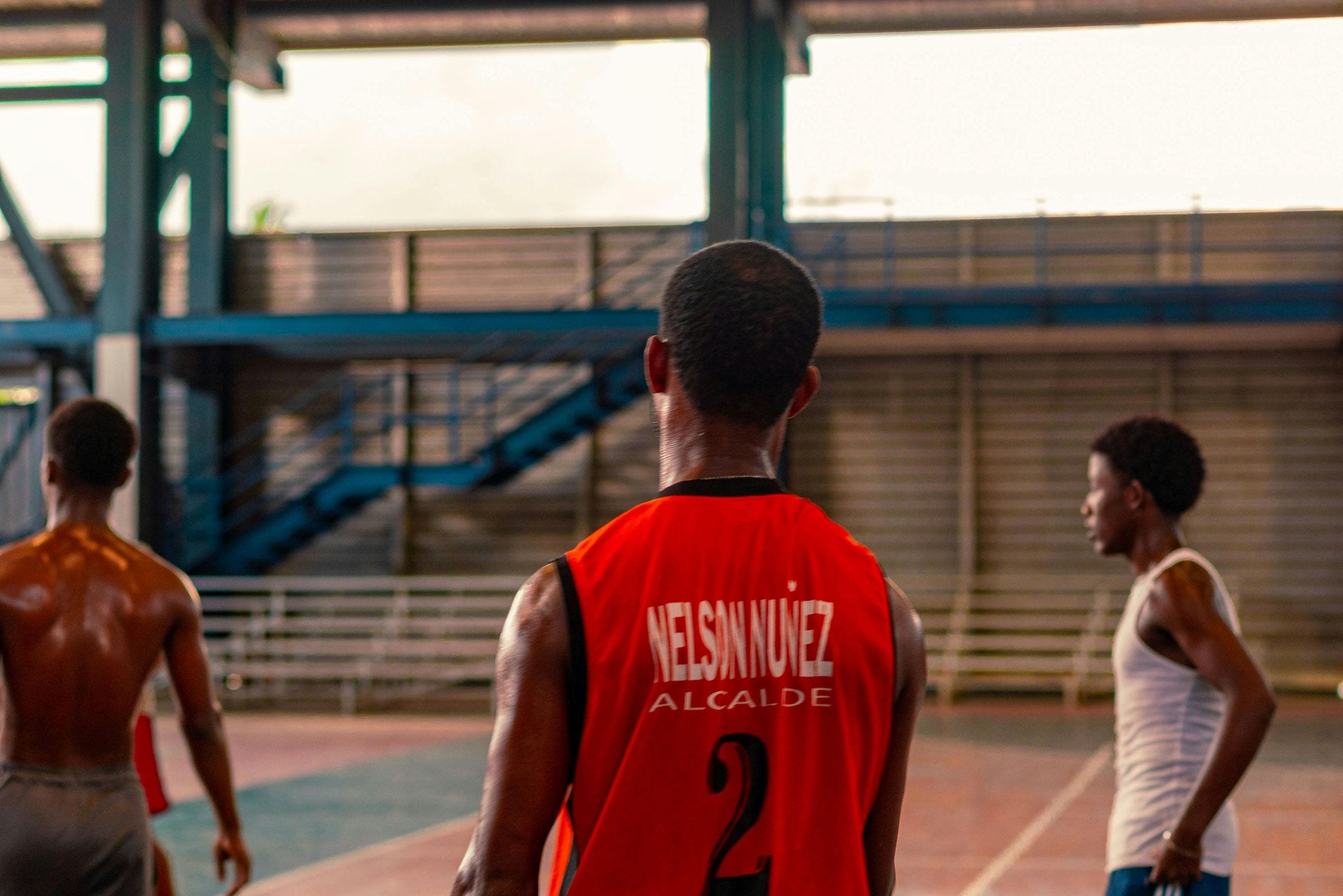 Young men on a basketball court at dusk, one in a red number-two jersey