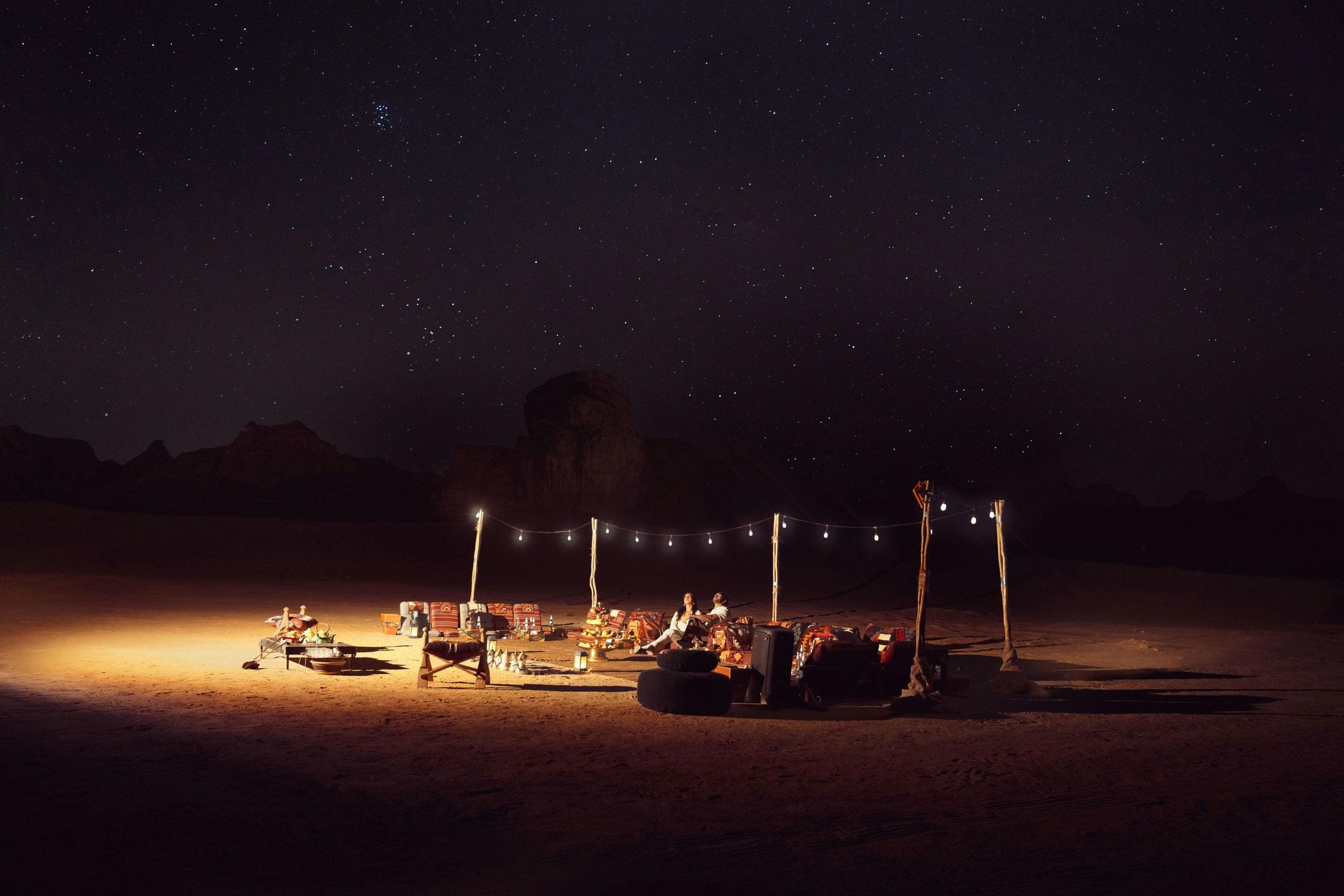 Couple relaxing at a lantern-lit desert camp under starlight