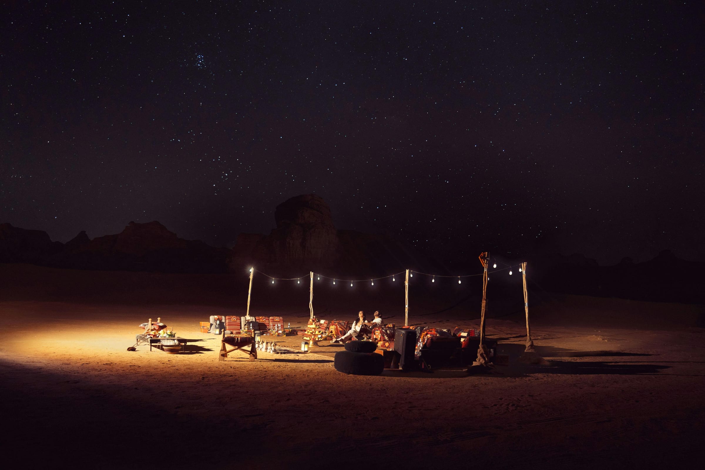 Couple relaxing at a lantern-lit desert camp under starlight