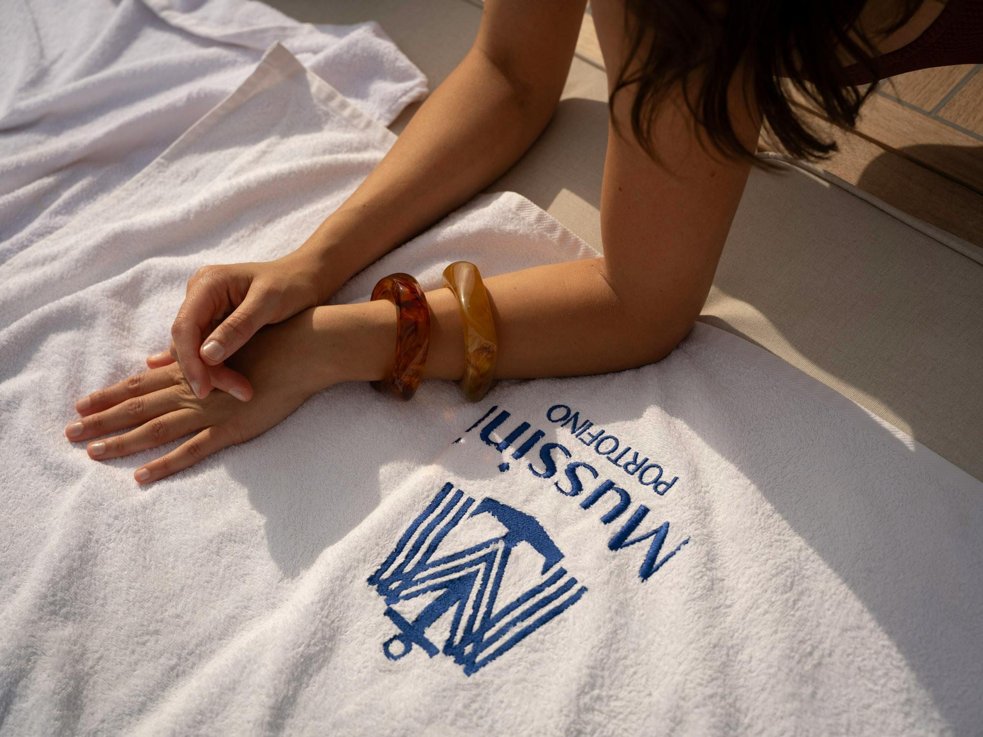 Woman's arm with amber bangles resting on a Mussini Portofino embroidered towel