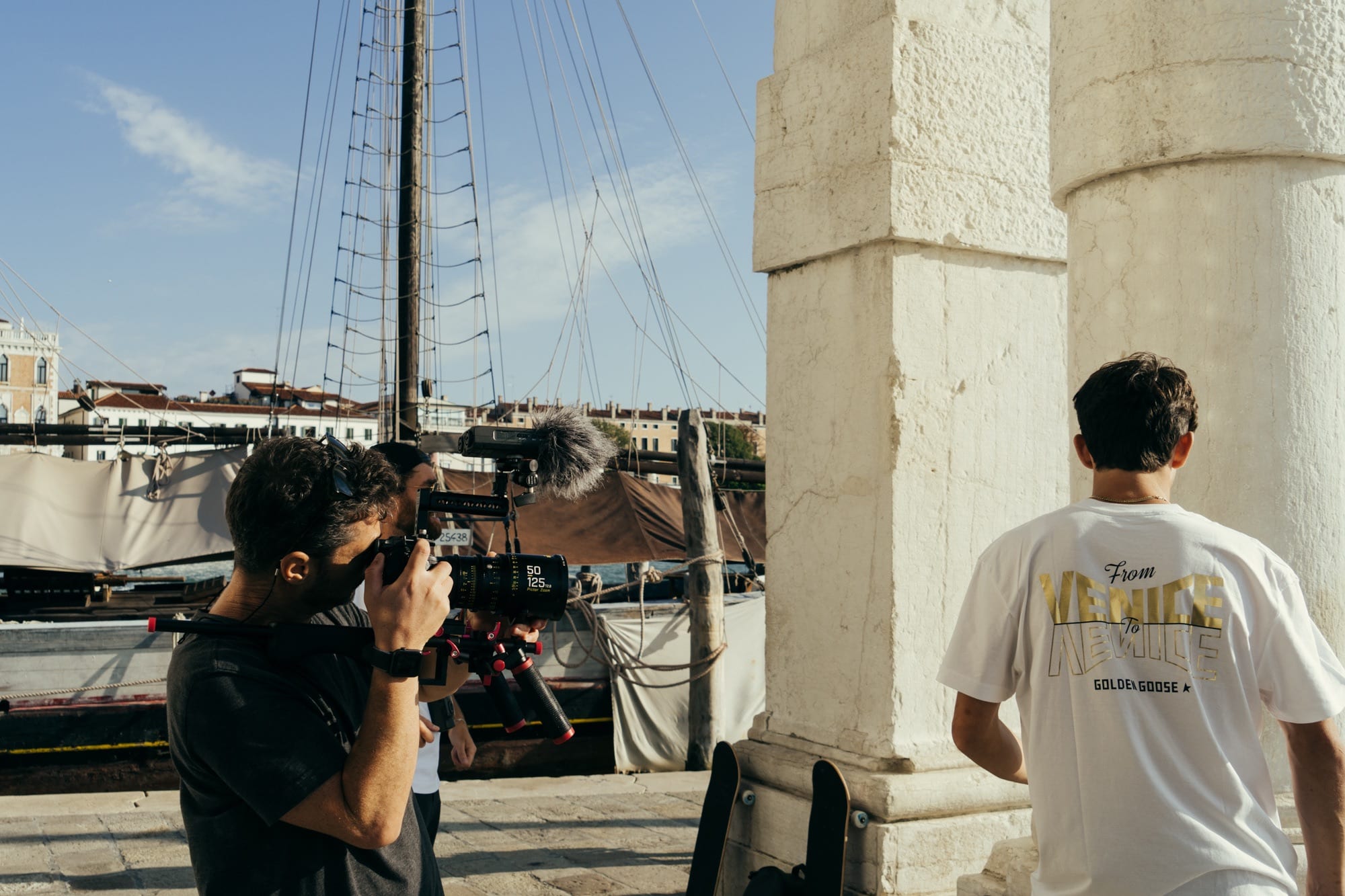 Behind the scenes: a camera operator films beside a crew member in a From Venice to Venice Golden Goose shirt
