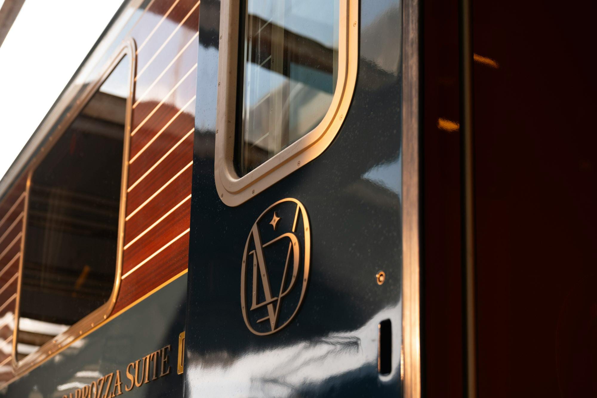 Close-up of the train's glossy blue carriage with gold monogram and Carrozza Suite lettering