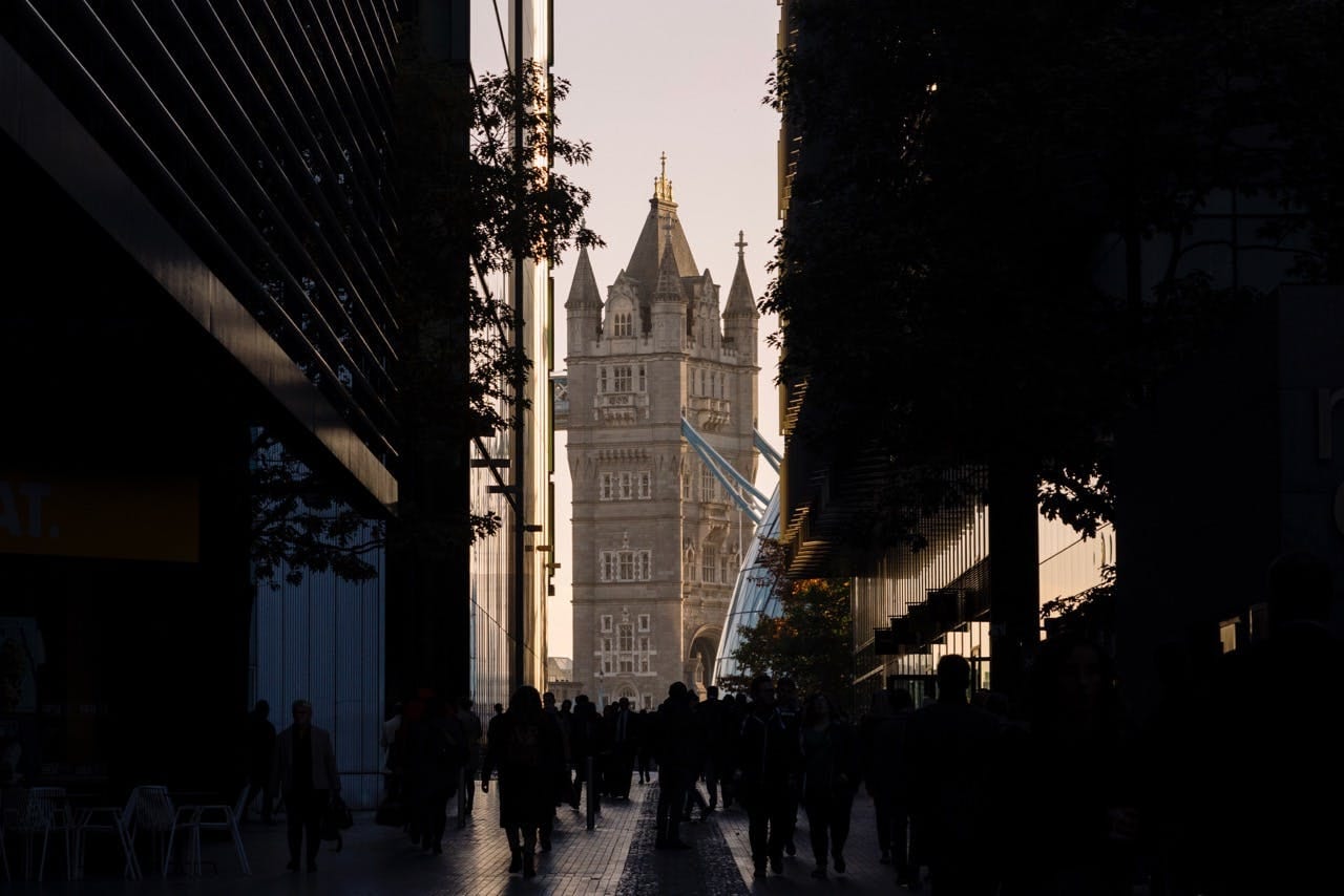 Tower Bridge glowing at the end of a shadowed street as commuters pass
