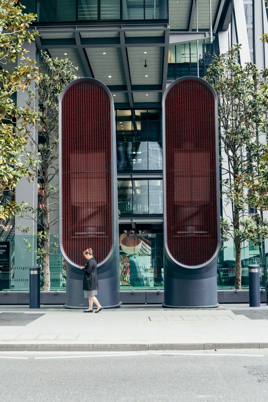 Woman walking past a towering red-lit louvred facade of a City office building