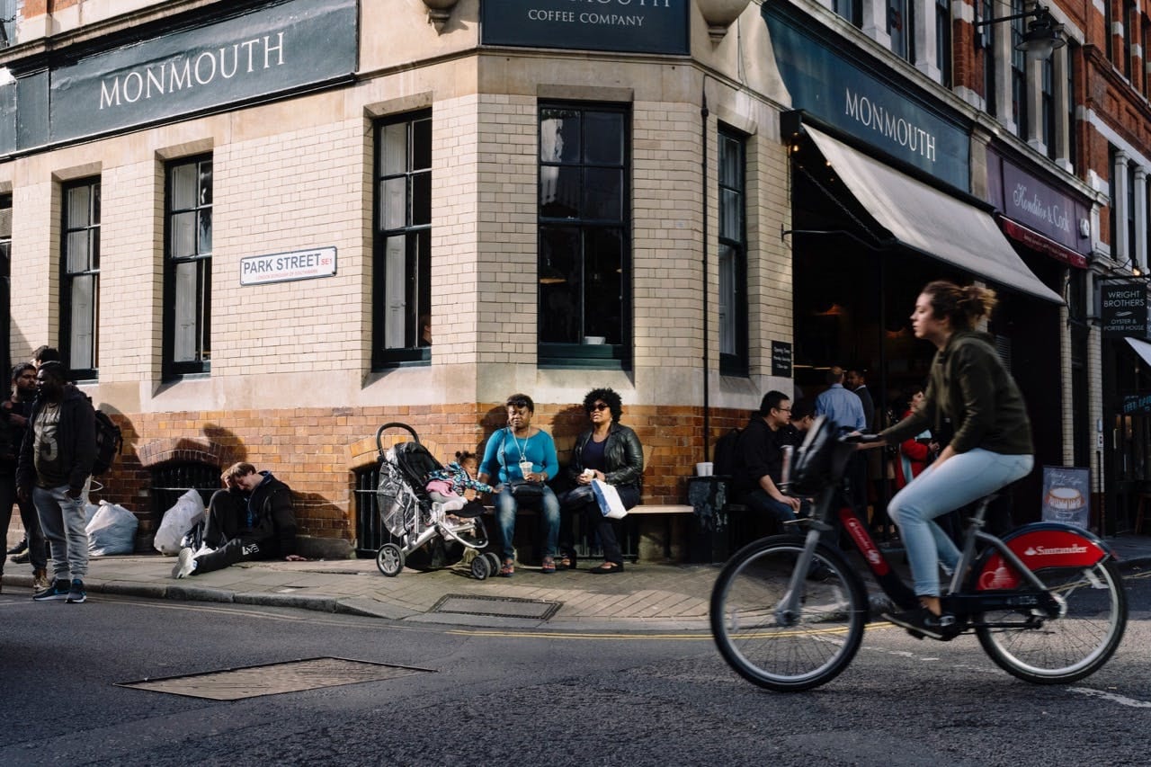 Cyclist passing Monmouth Coffee Company on a sunlit Park Street corner